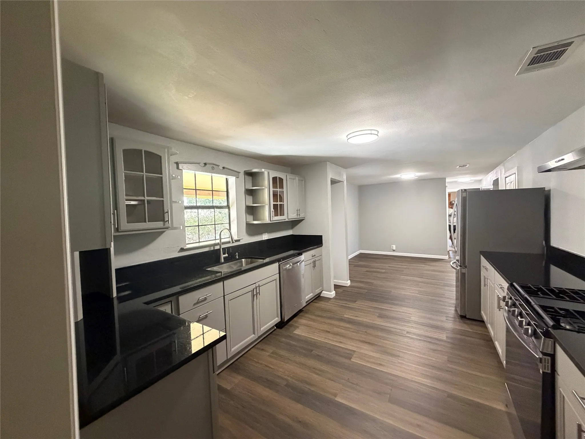 Kitchen featuring dark Granite countertops, light gray cabinetry with some glass-front uppers, stainless steel appliances, wood-finish flooring, and recessed lighting