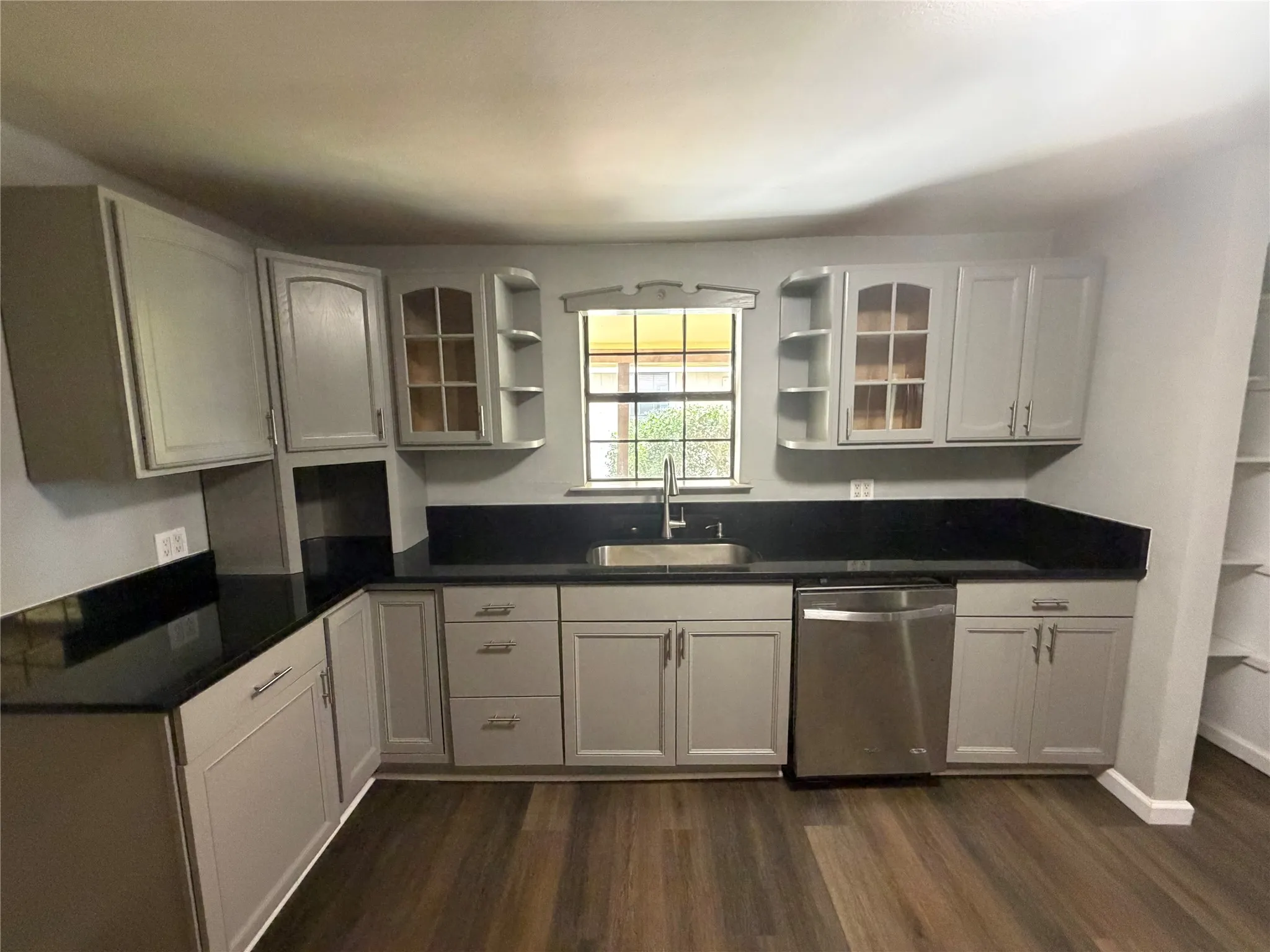 Kitchen featuring grey cabinetry, dark countertops, a stainless steel sink, a stainless steel dishwasher, and wood-finish flooring