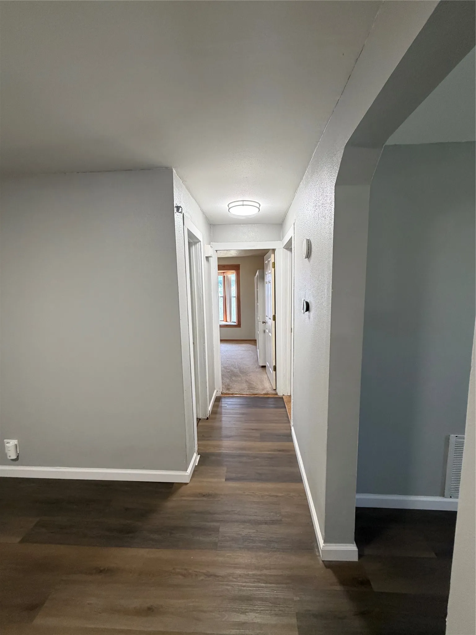 Hallway featuring wood-finish flooring, light gray wall paint, white trim, and an overhead flush-mount light fixture