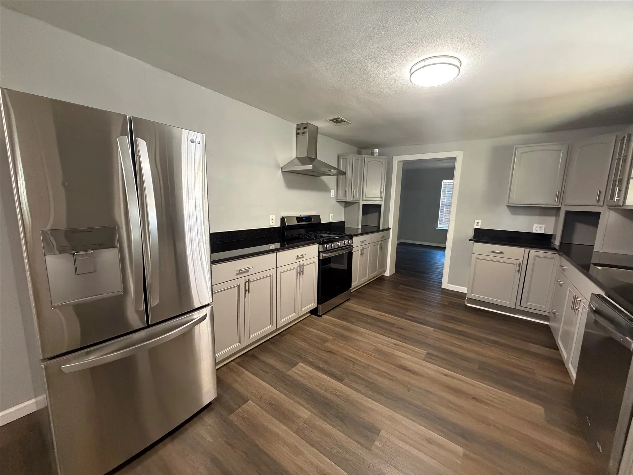 Kitchen featuring wood-finish flooring, stainless steel appliances, dark countertops, and light-toned cabinetry