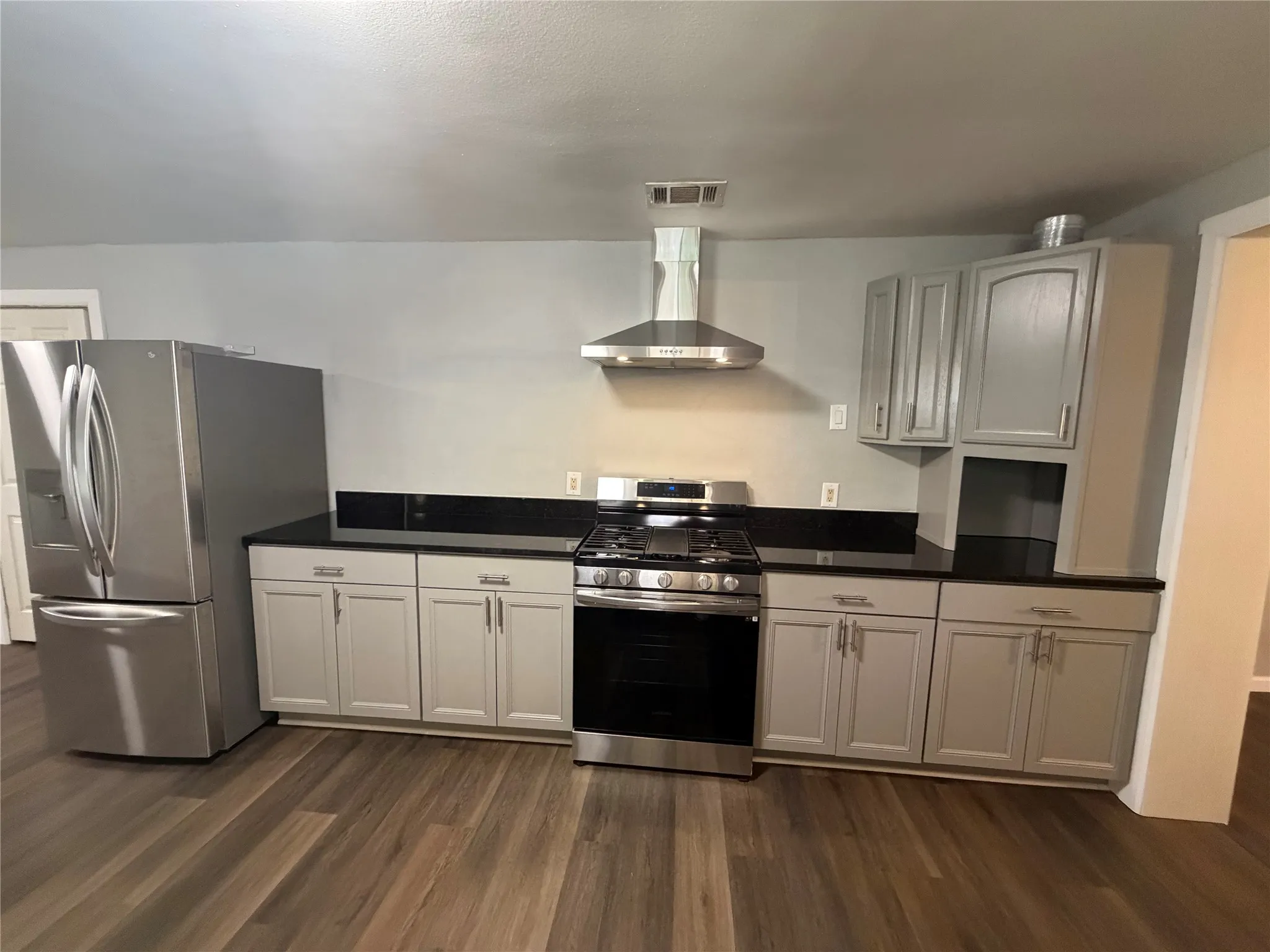 Kitchen featuring wood-finish flooring, stainless steel appliances, dark countertops, and light gray cabinetry