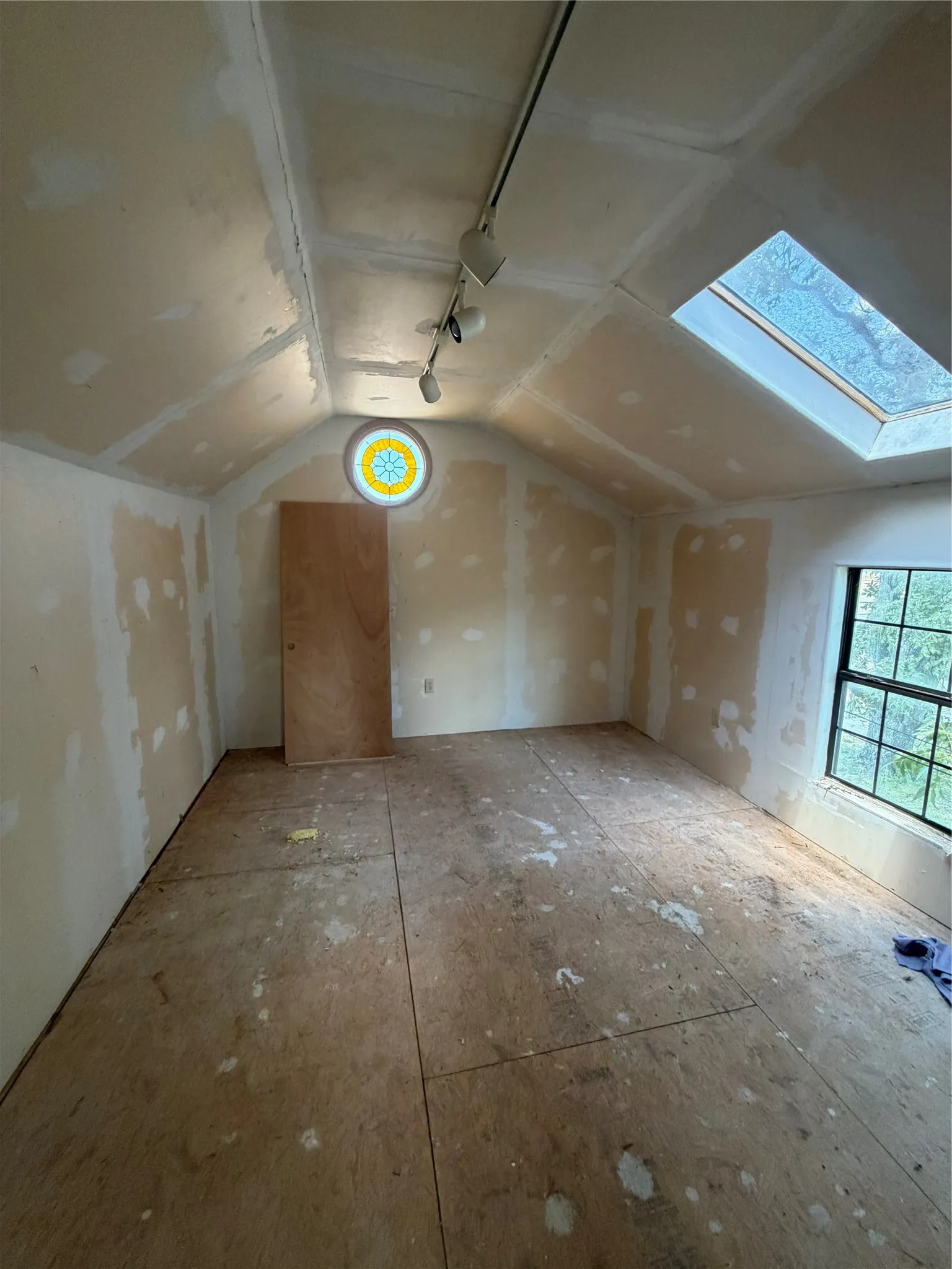 Sloped ceiling room featuring track lighting, a circular stained-glass window, a skylight, and a large window