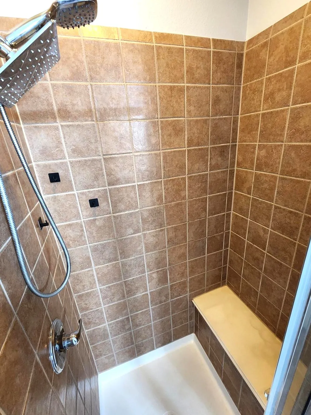 Tiled shower with a built-in bench, chrome showerhead, and handheld spray