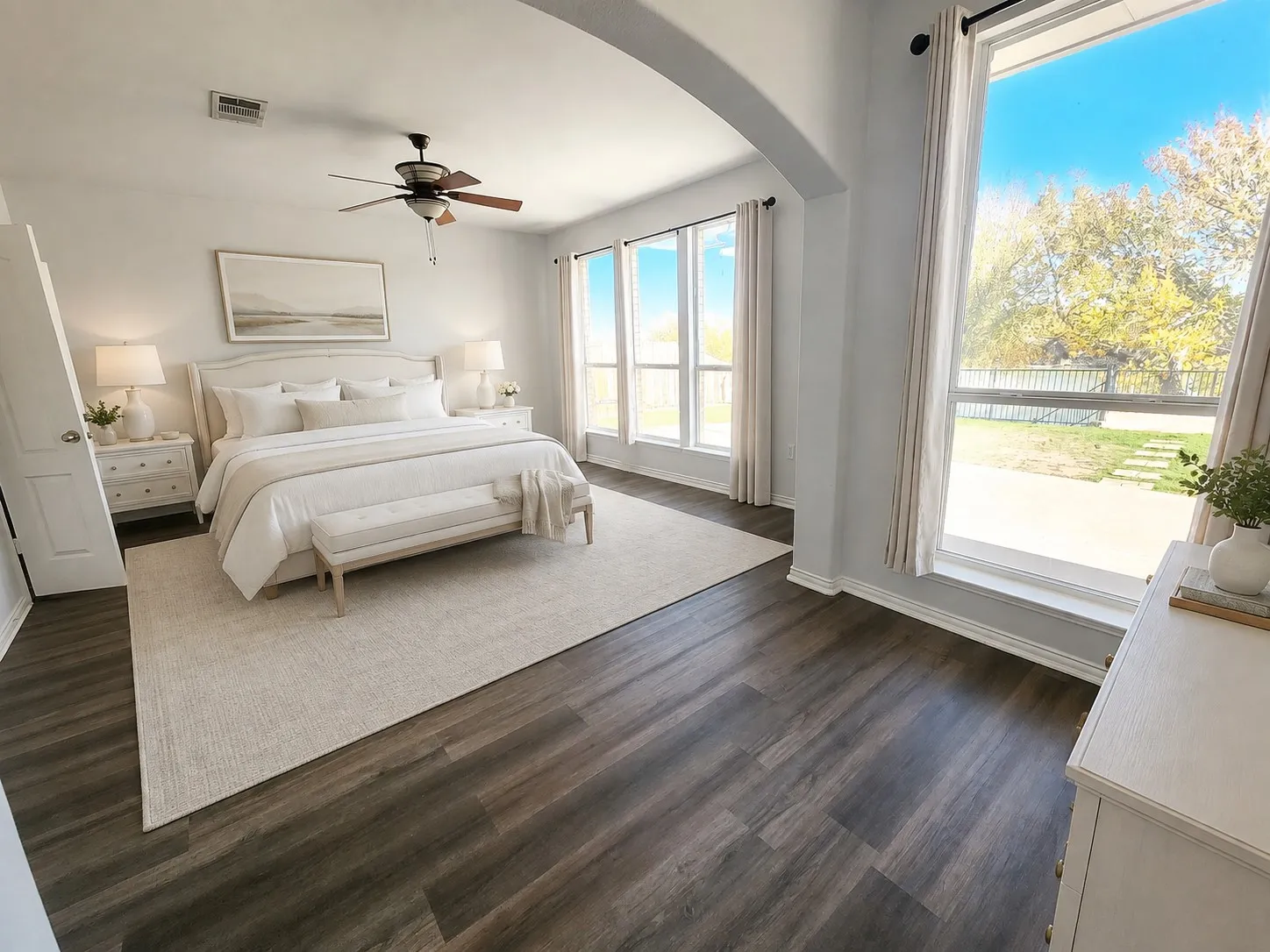 Expansive room featuring plank flooring, an arched entryway, a ceiling fan, and multiple tall windows