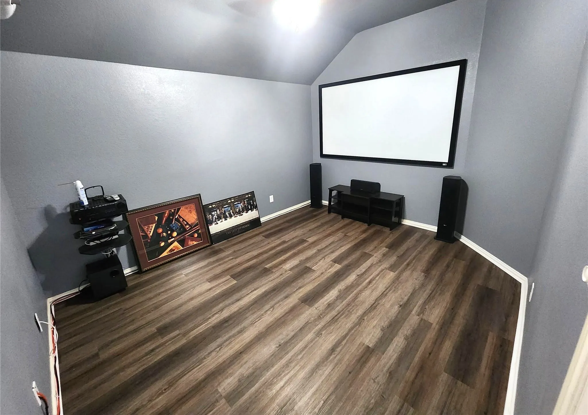 Plank flooring with neutral wall tones, vaulted ceiling, and a large projection screen