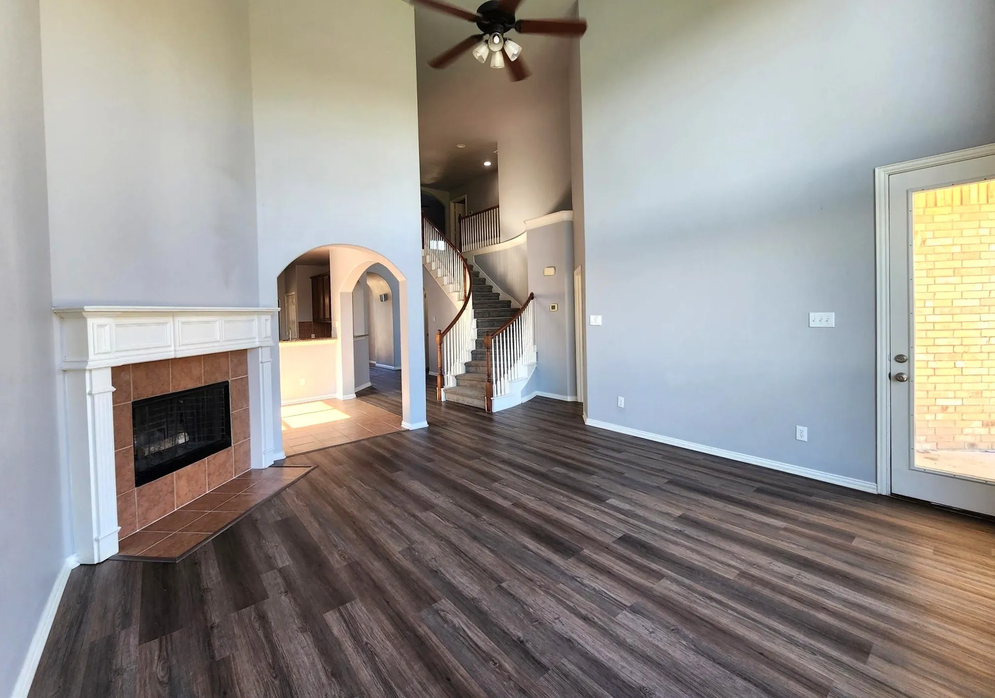 Plank flooring, a corner fireplace with a decorative mantel and tile surround, a ceiling fan, a full-light exterior door, and an arched entryway