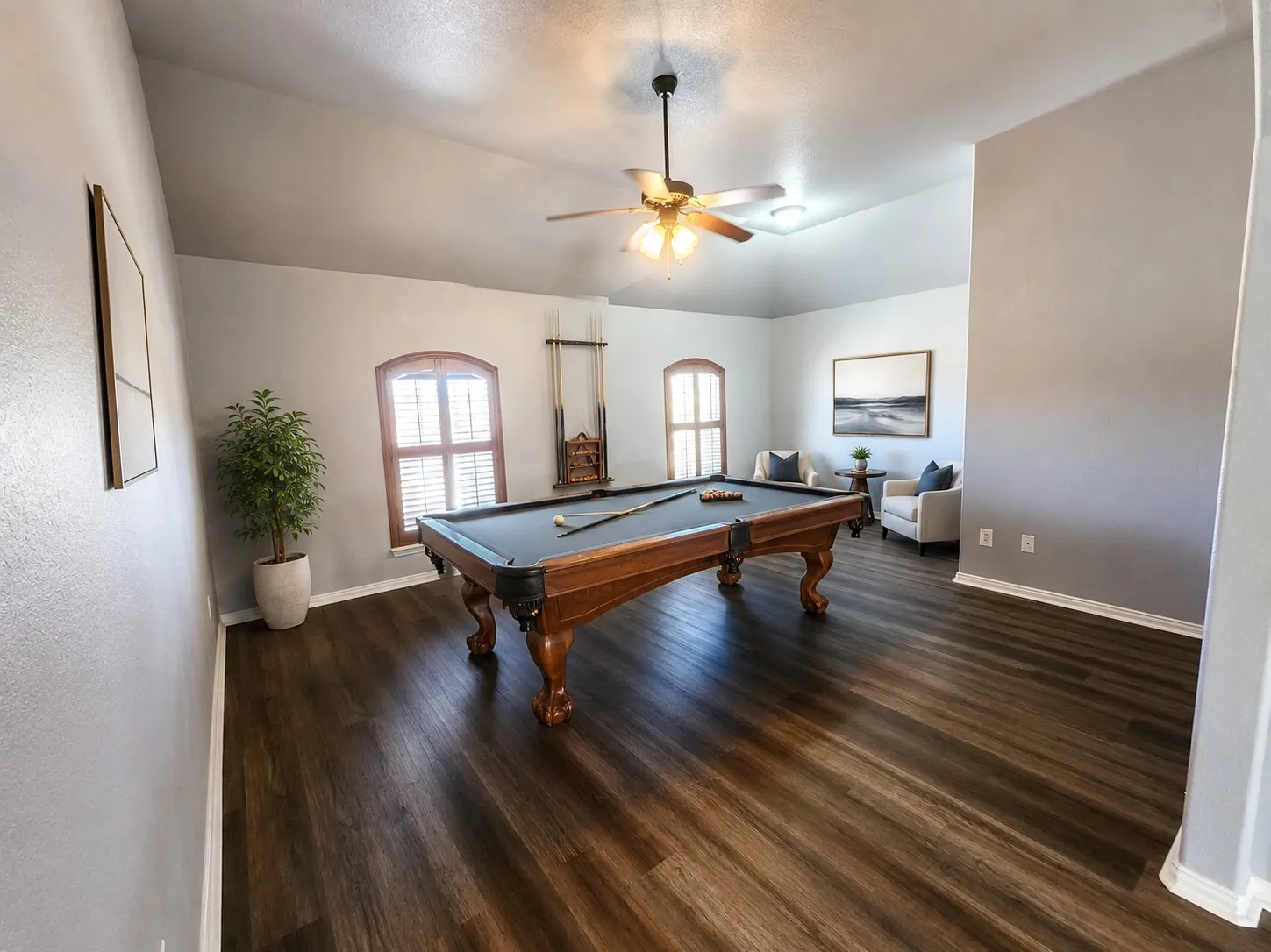 Vaulted ceiling with a ceiling fan, plank flooring, two arched windows with plantation shutters, and a recessed lighting fixture