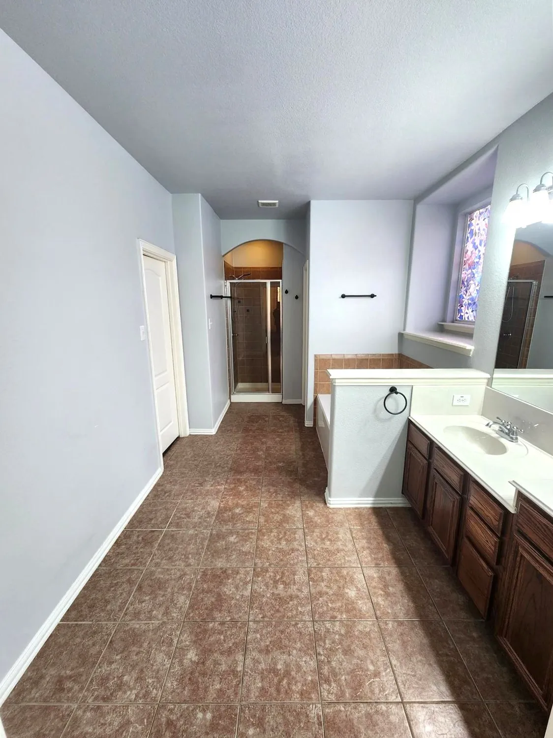 Bathroom featuring tile flooring, a built-in soaking tub, a dual-sink vanity with wood cabinetry, and a glass-enclosed shower