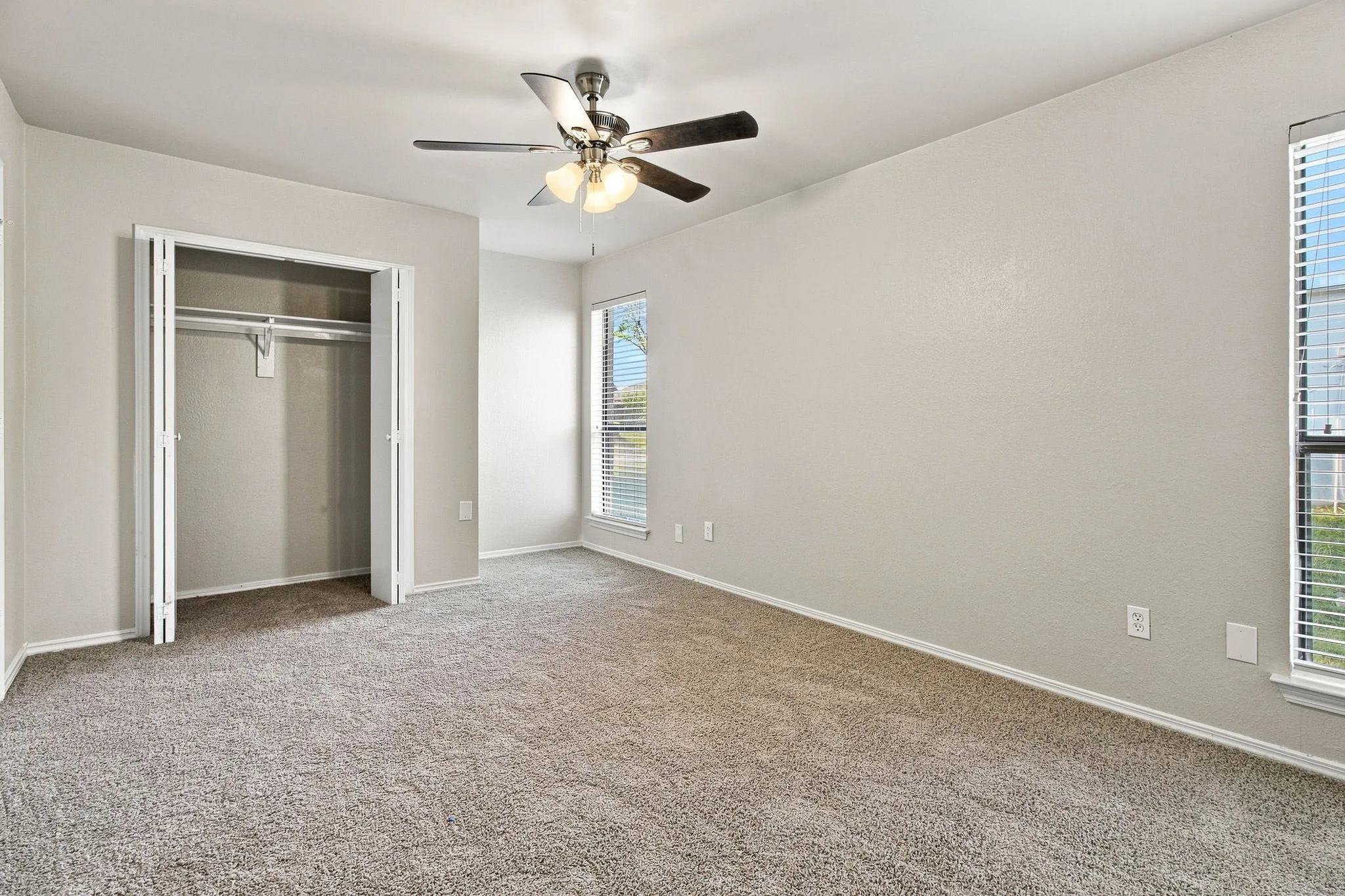 Neutral wall tones, ceiling fan with integrated lighting, window with blinds, carpeted flooring, and a bi-fold door closet