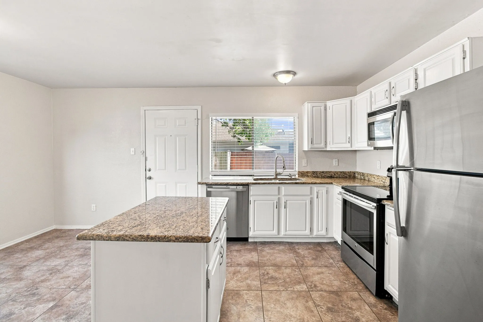 Kitchen featuring a central island, white cabinetry, granite countertops, stainless steel appliances, and tiled flooring