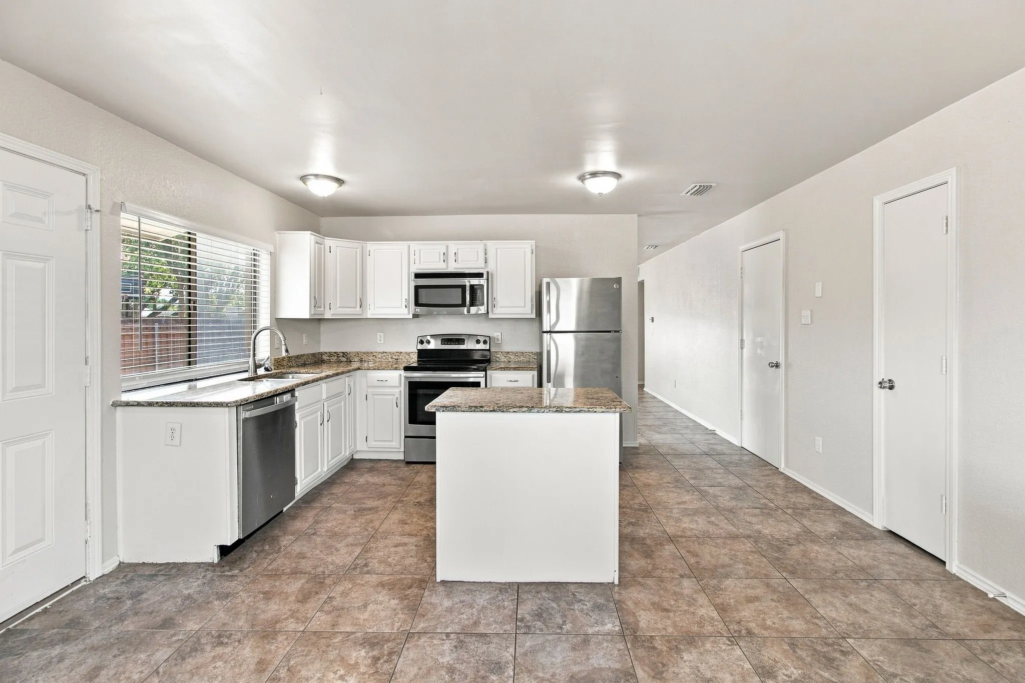 Kitchen featuring white cabinetry, a central island, stainless steel appliances, granite-style countertops, and tile flooring