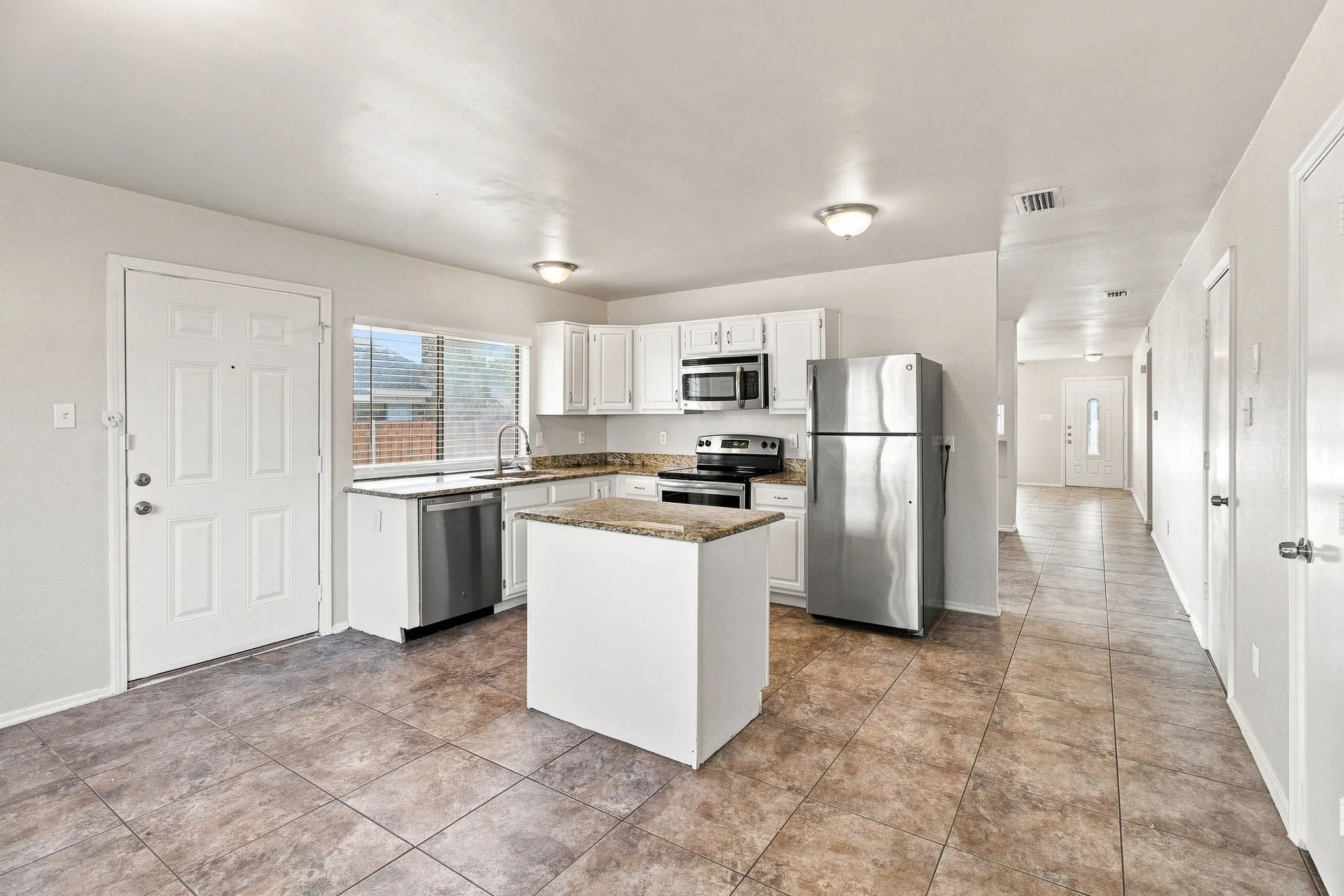 Kitchen featuring white cabinetry, stainless steel appliances, a center island, and tile flooring