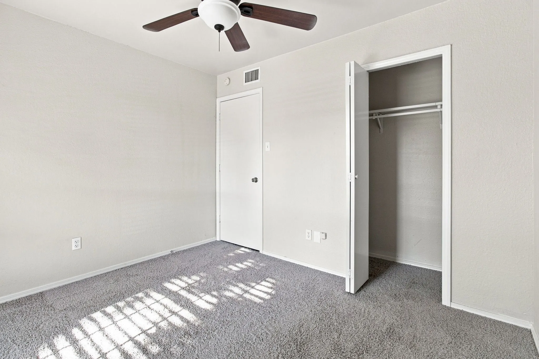 Neutral-toned walls, ceiling fan, grey carpet flooring, and an open closet with hanging rods
