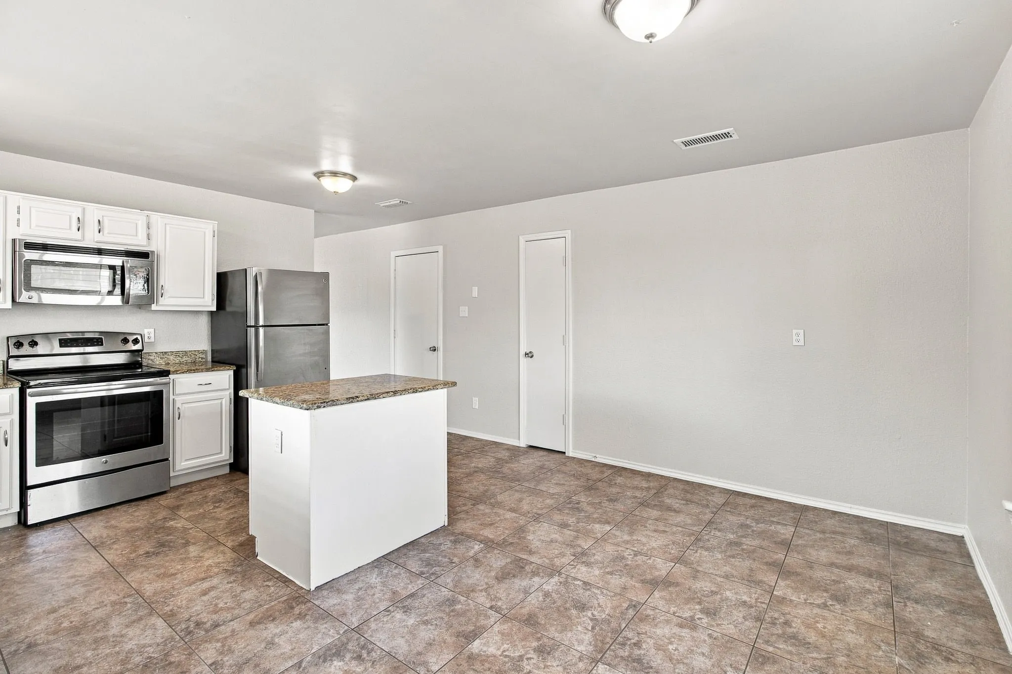 Kitchen featuring white cabinetry, stainless steel appliances, a kitchen island with a stone-finish countertop, and tile flooring