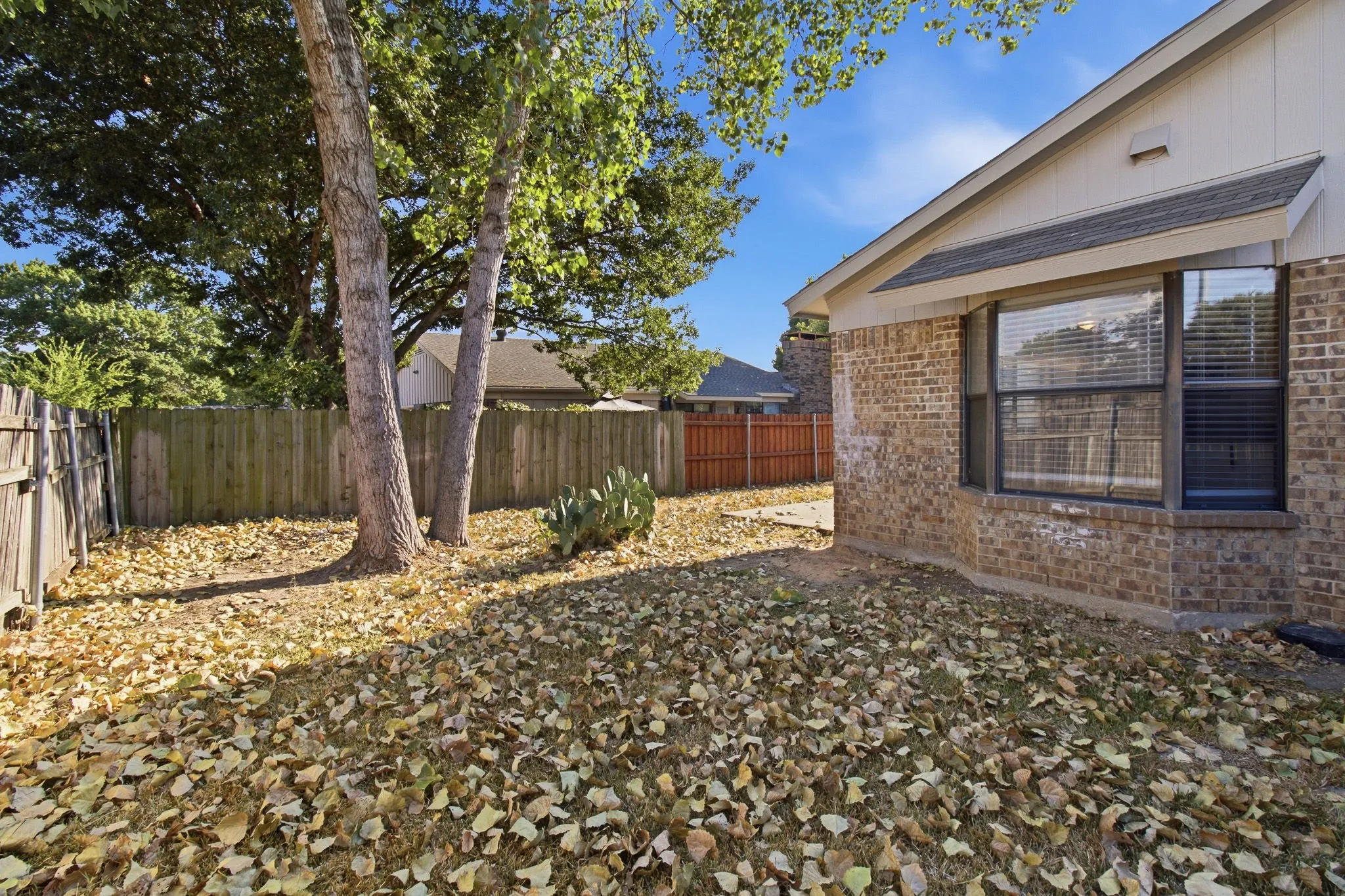 Brick exterior, wood fencing, mature trees, bay window, and a gabled roofline