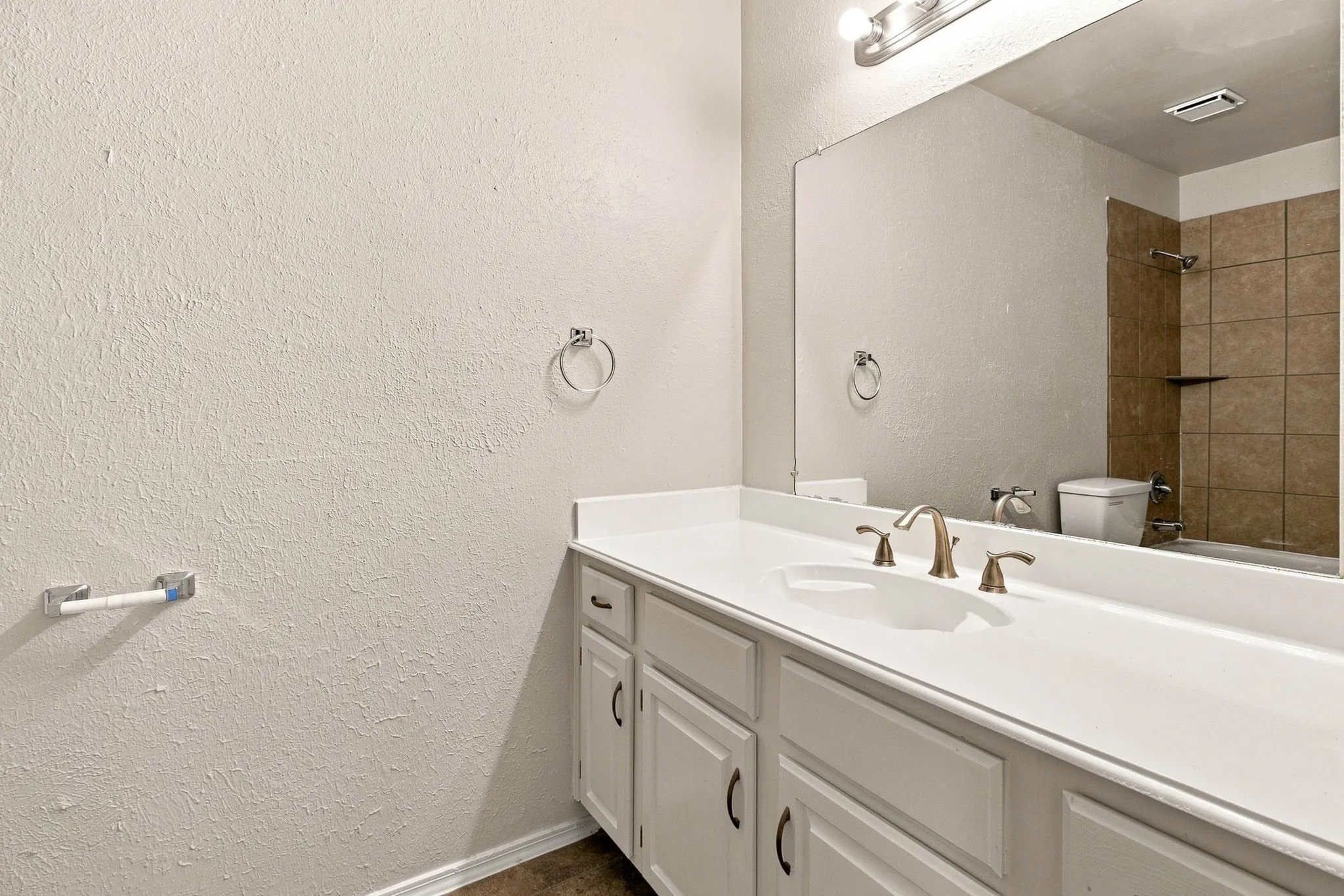 White vanity with integrated sink, bronze-finish faucet, and a large wall mirror
