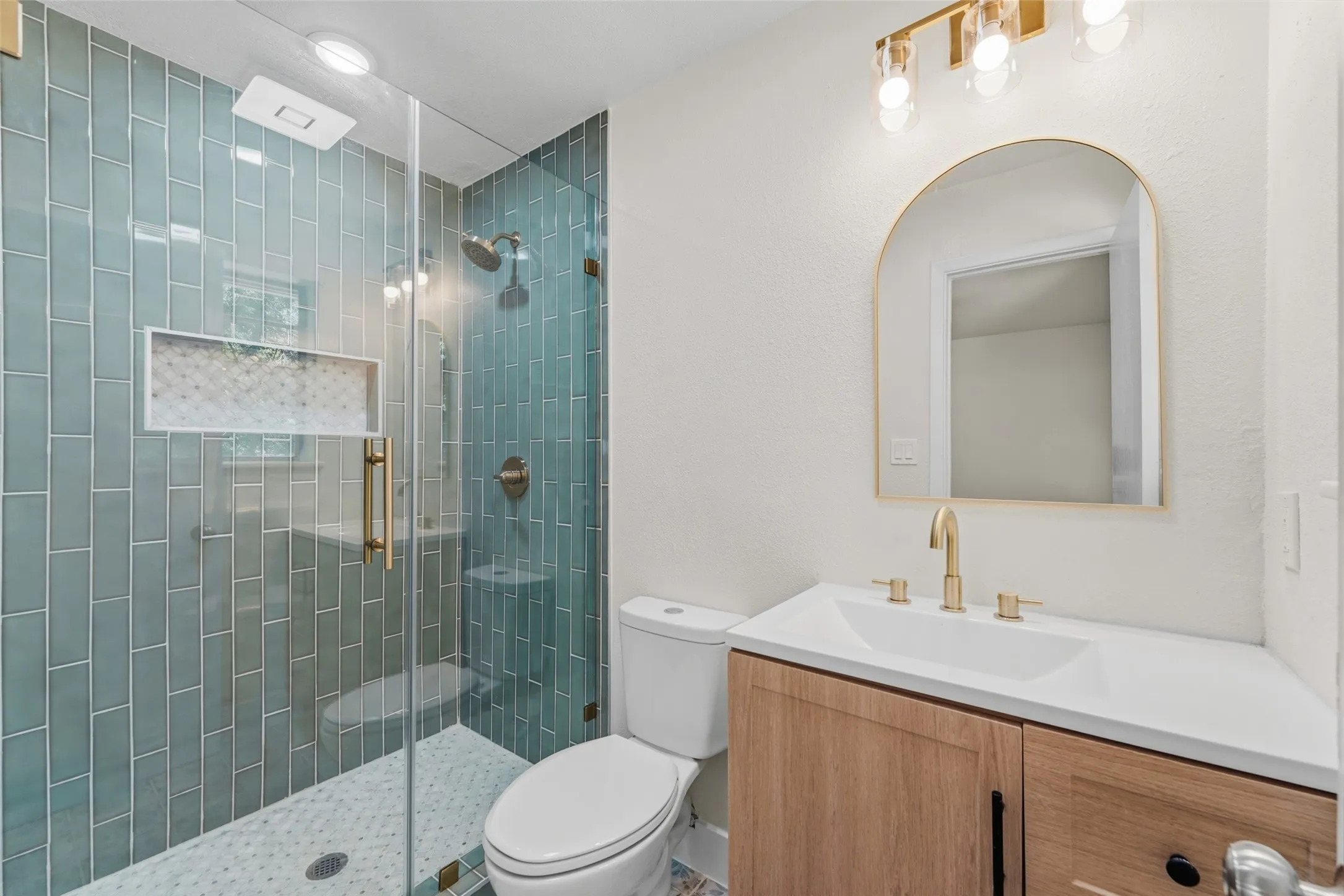 Glass-enclosed shower with subway tile surround, built-in niche, and gold-finish fixtures