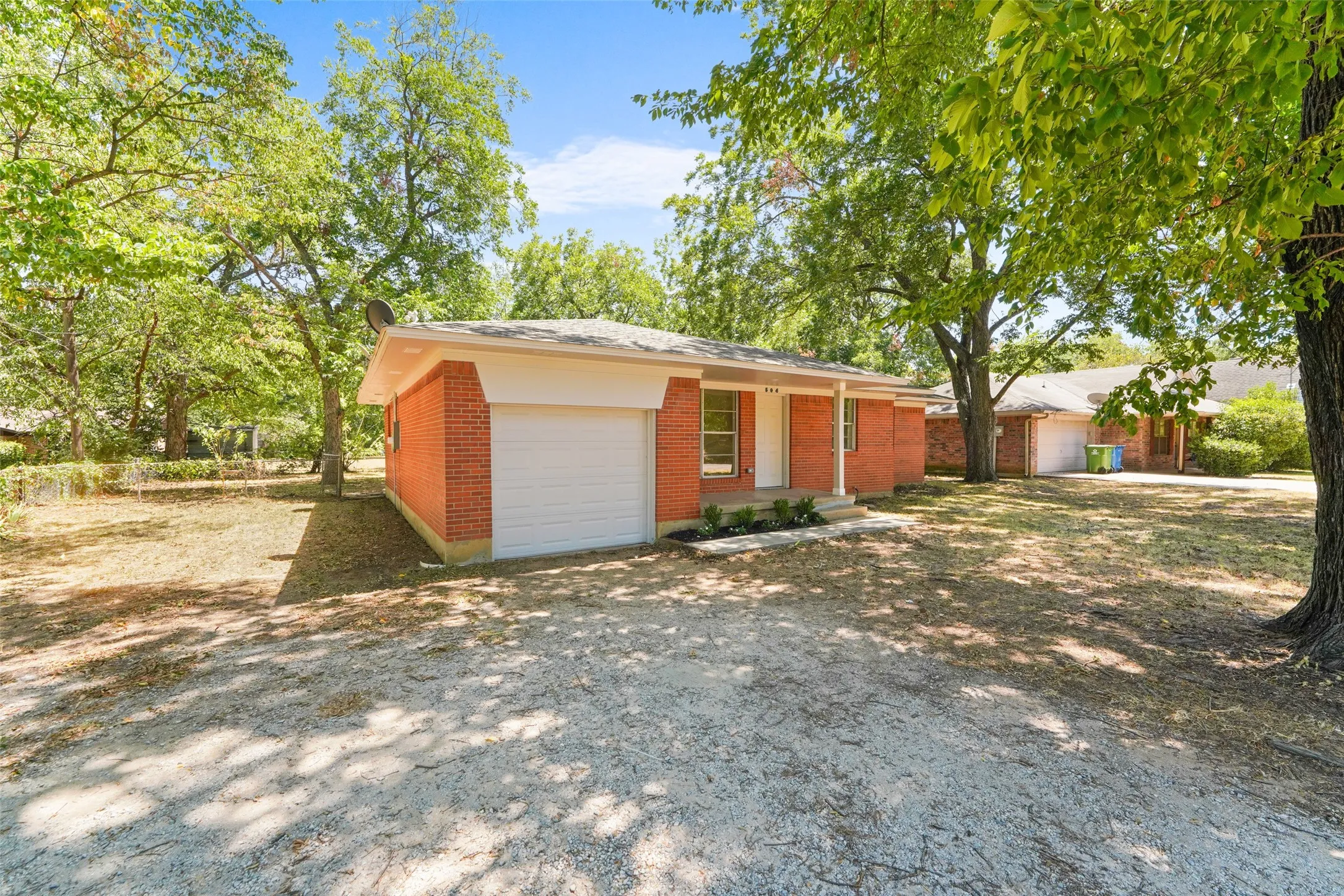 Brick exterior with an attached garage, covered front entry, and mature trees