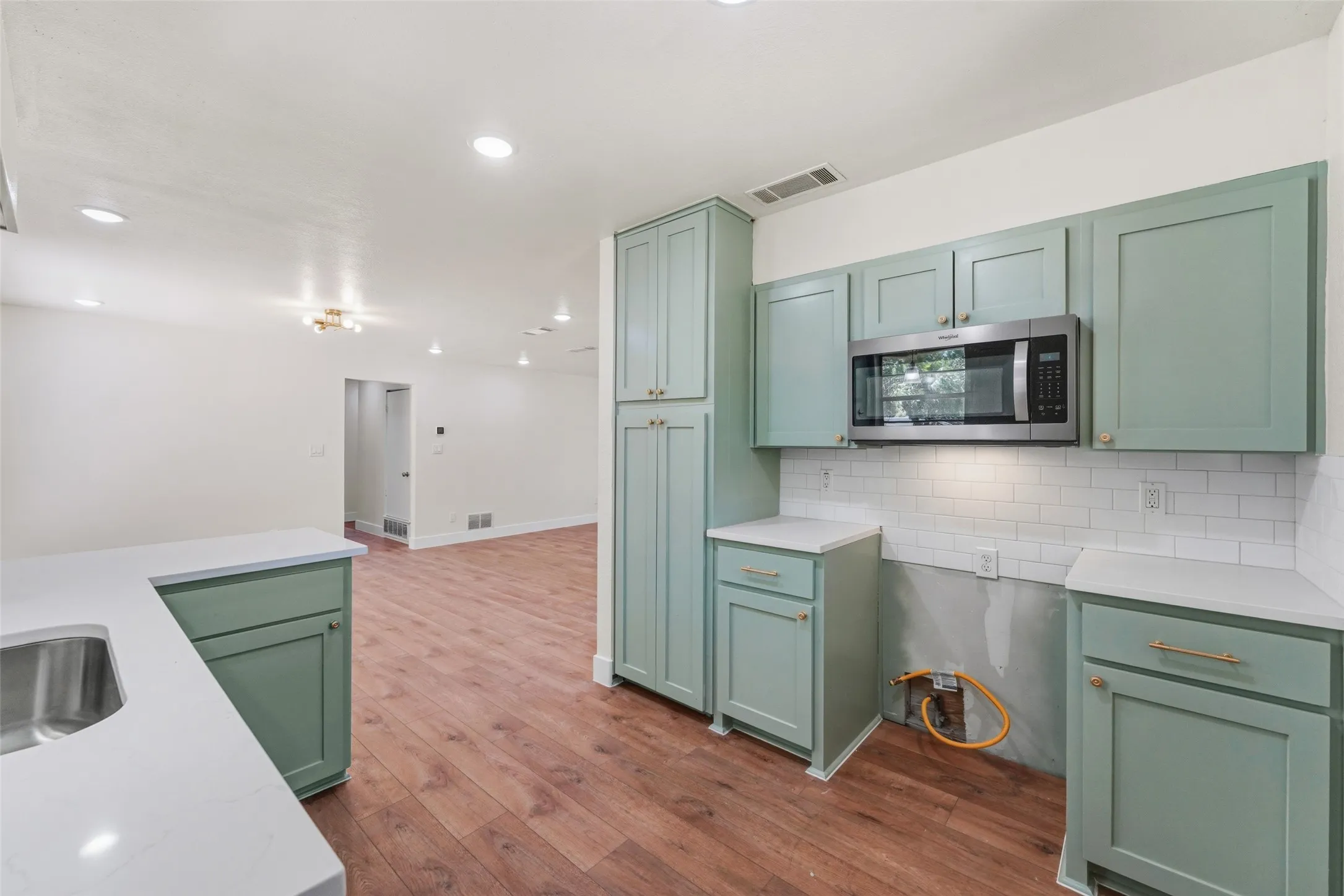 Kitchen featuring wood-finish flooring, mint green cabinetry, stainless steel microwave, white subway tile backsplash, and recessed lighting