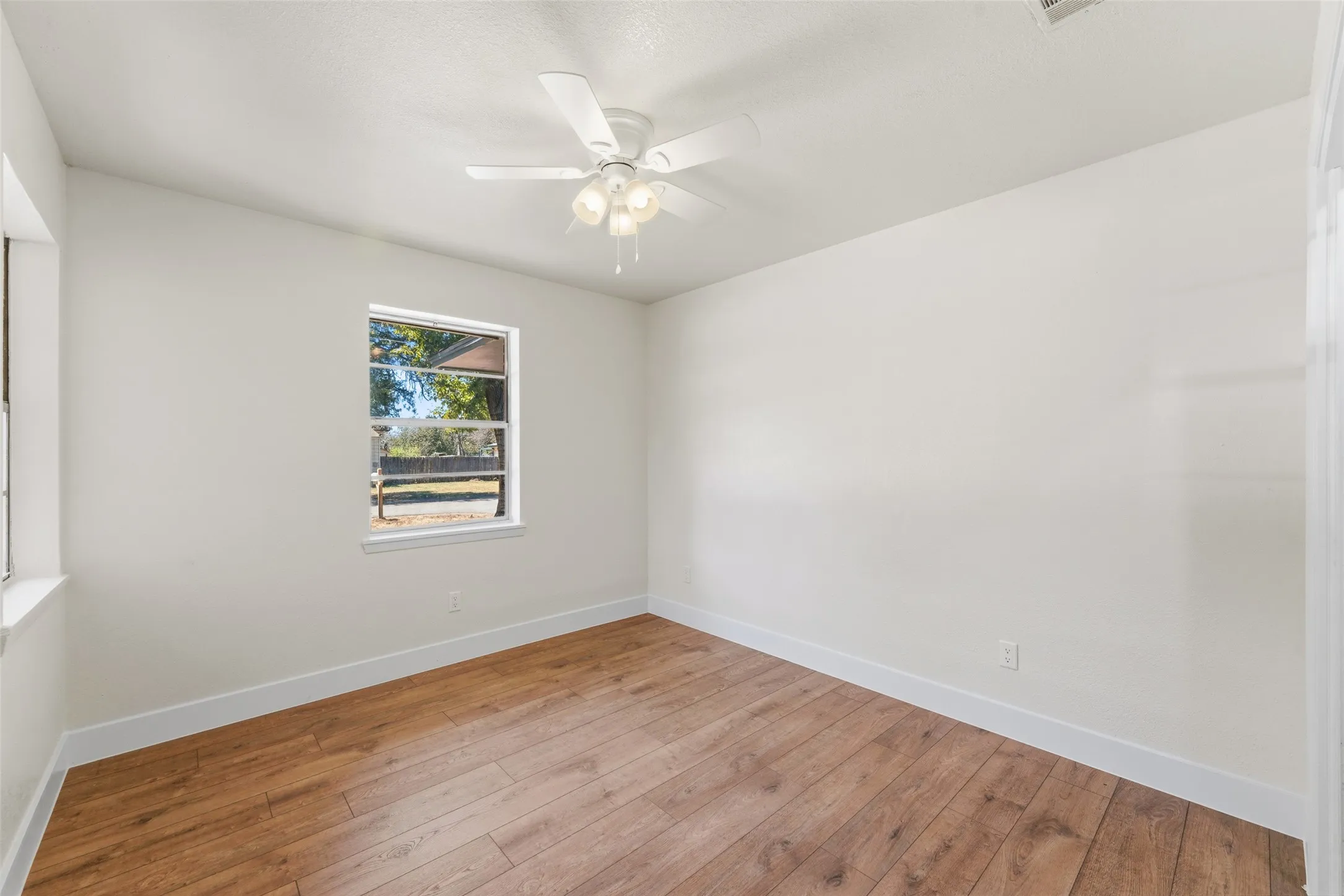 Wood-finish flooring, white walls, and a ceiling fan with integrated lighting