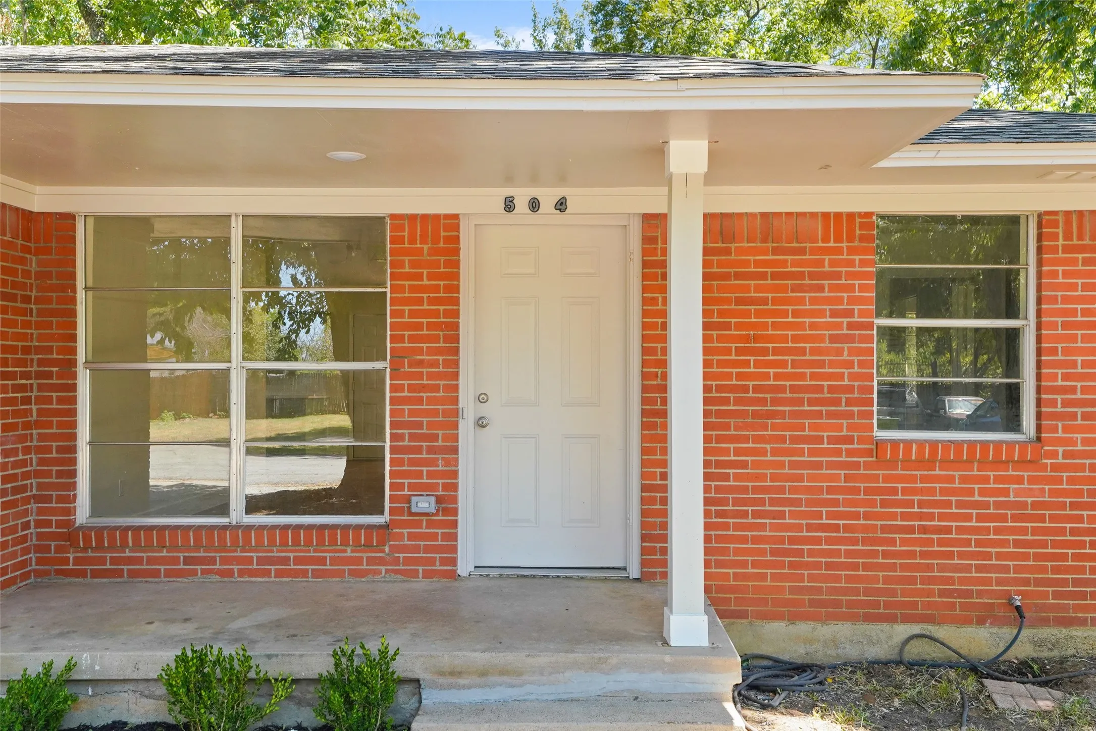 Brick exterior with a covered entry, white front door, and multiple windows