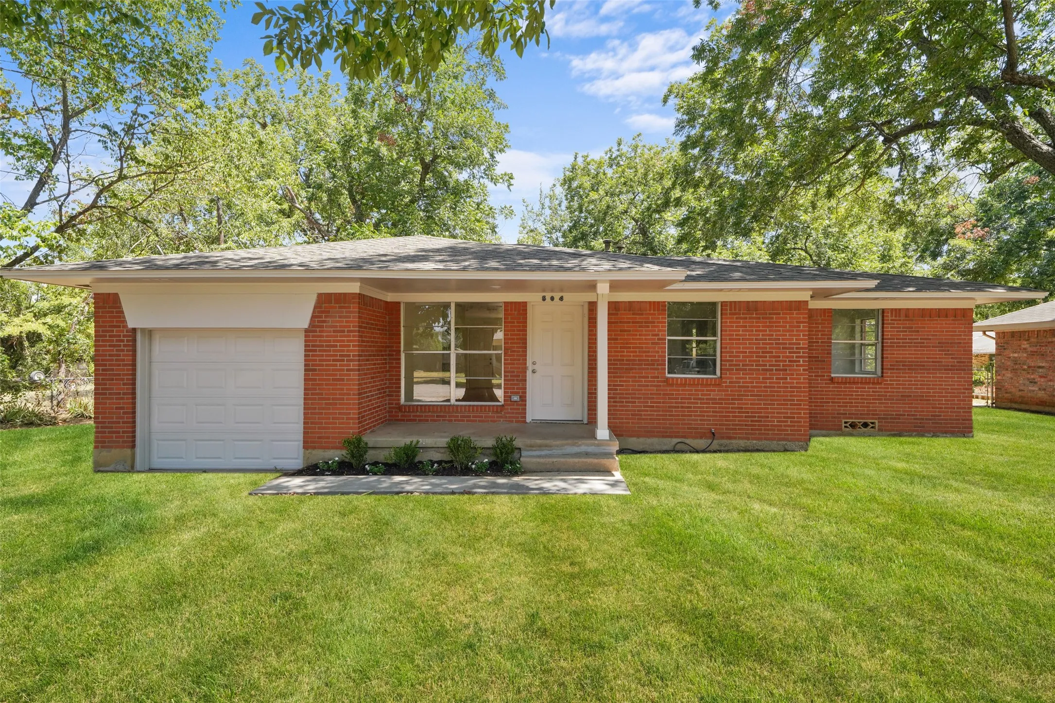 Brick exterior with a covered entry, attached garage, and mature tree canopy