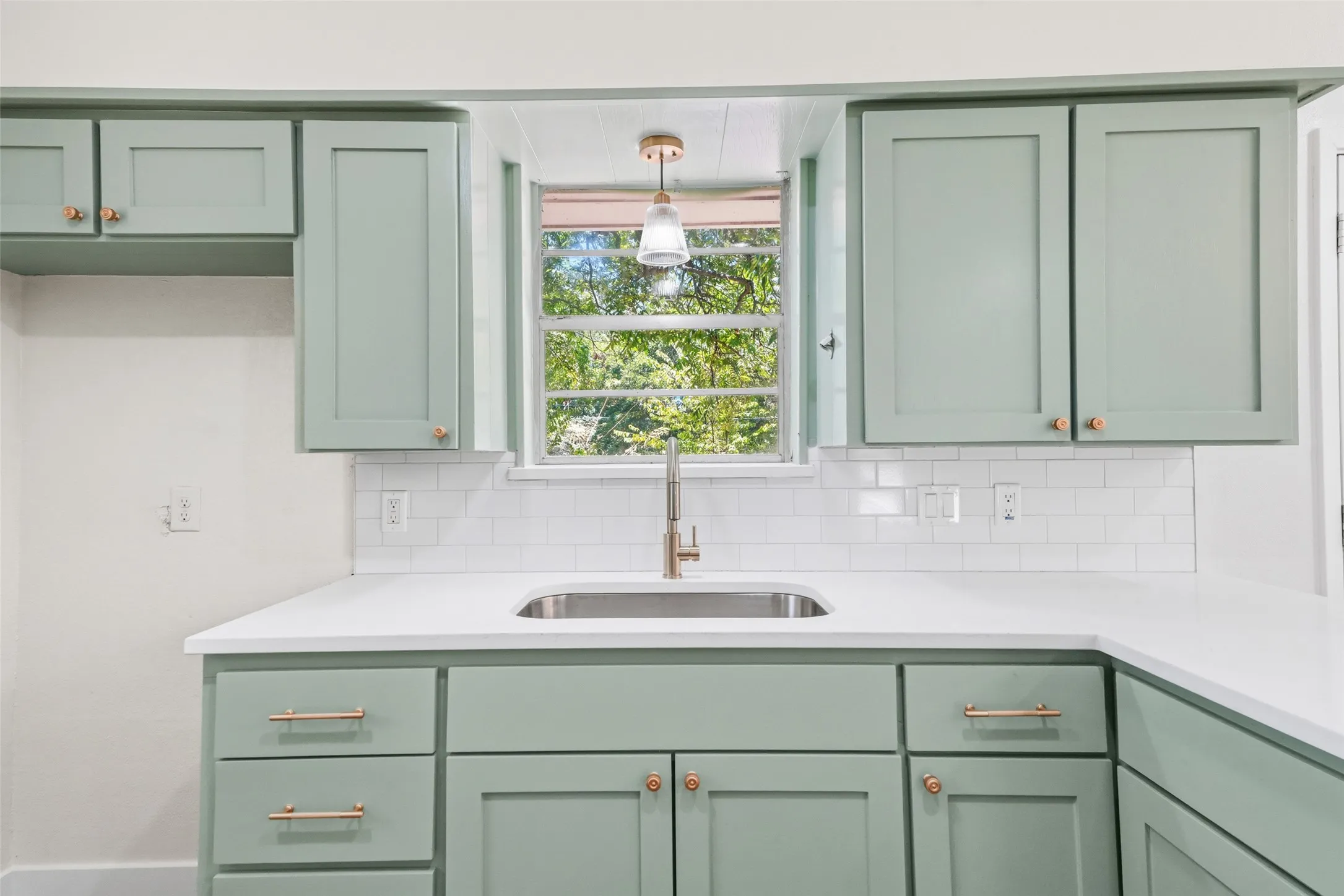 Custom cabinetry with gold-tone hardware, white countertop, stainless steel sink, and subway tile backsplash