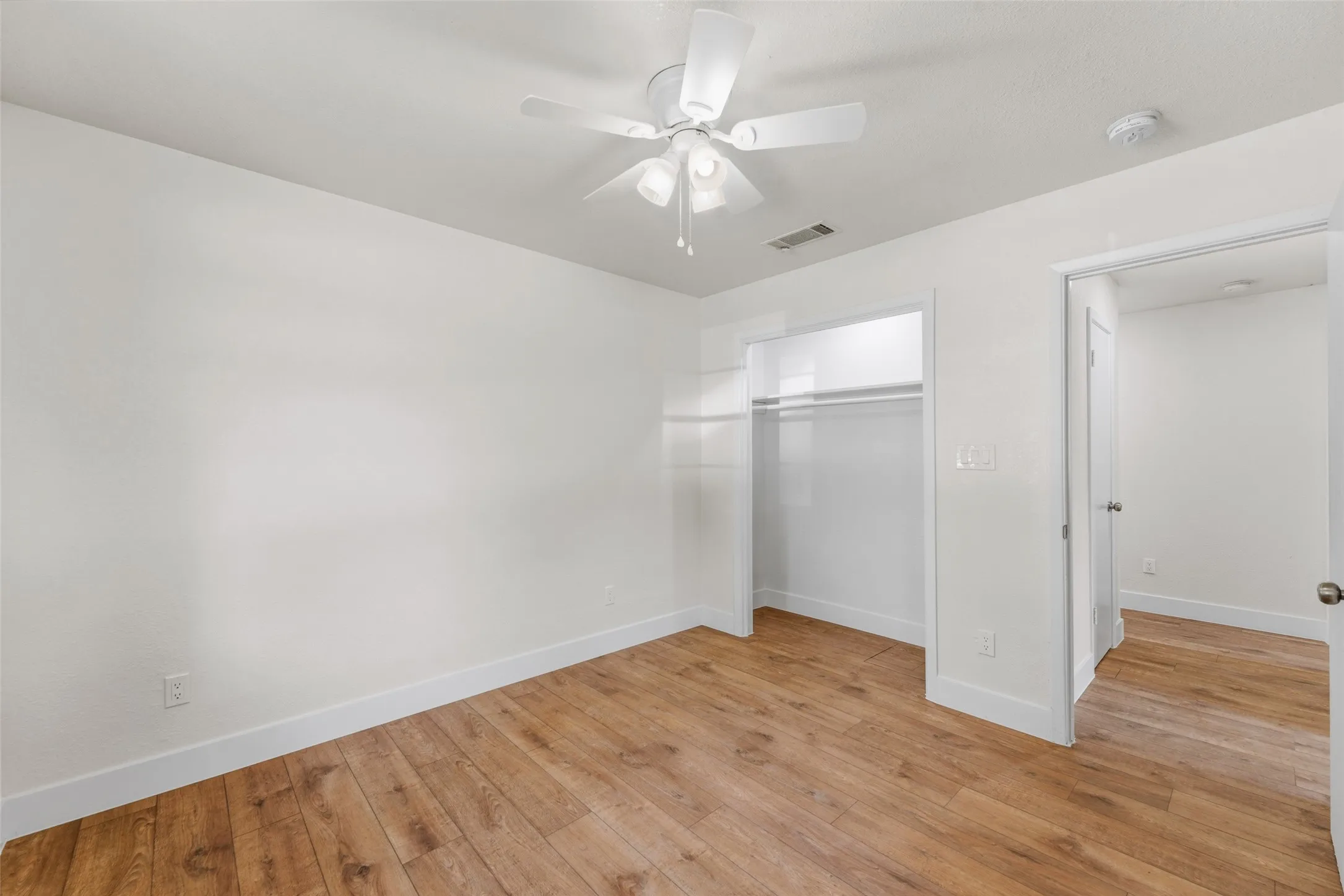 Wood-finish flooring, white walls, and a ceiling fan