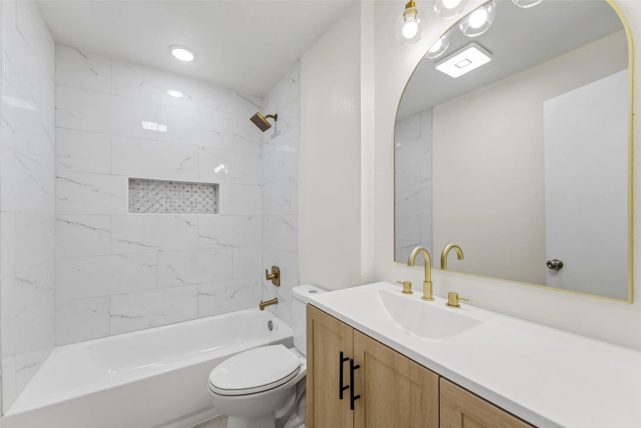 Bathroom featuring a tub/shower combination with white tile surround, mosaic shower niche, and gold-finish fixtures