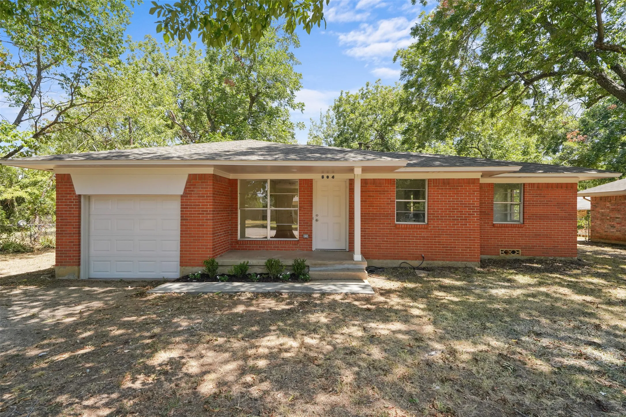 Brick exterior with a single-car garage, covered entry, and mature trees