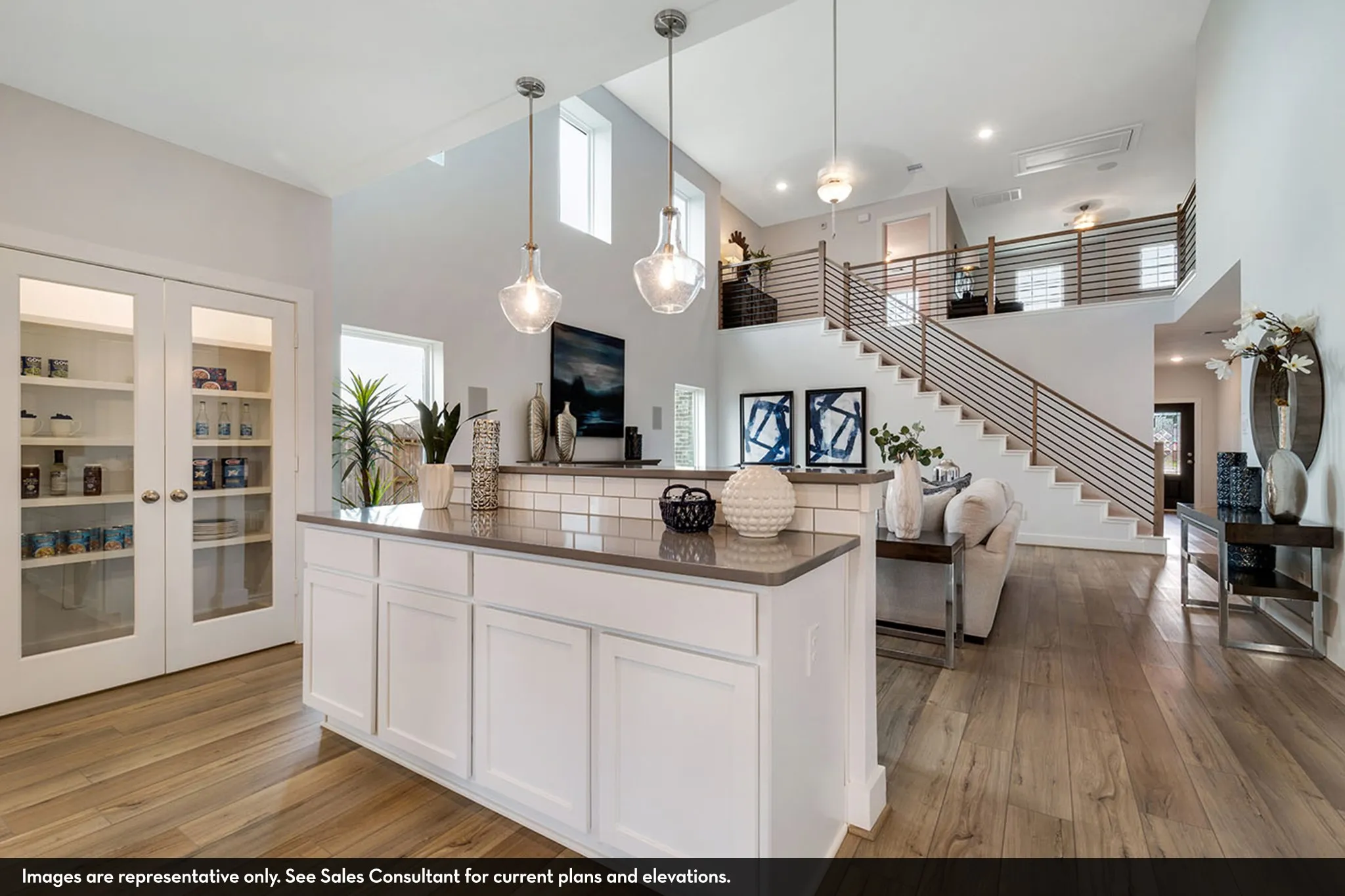 Open-concept living space featuring wood-finish flooring, a two-story ceiling, a modern staircase with horizontal railings, a kitchen island with a countertop, and a built-in pantry with glass-paneled double doors