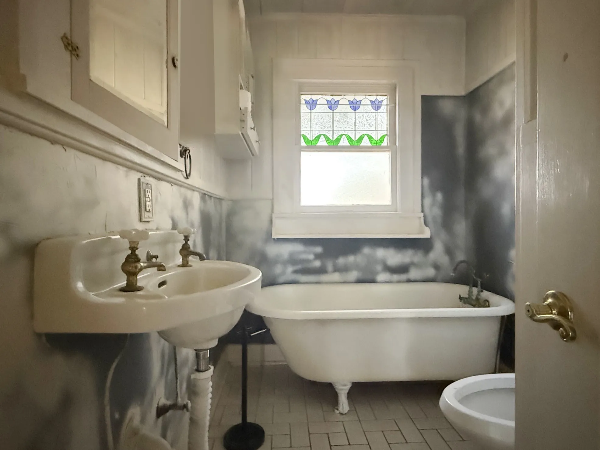 White porcelain pedestal sink with brass-finish fixtures, a clawfoot bathtub, and a window with stained glass detailing