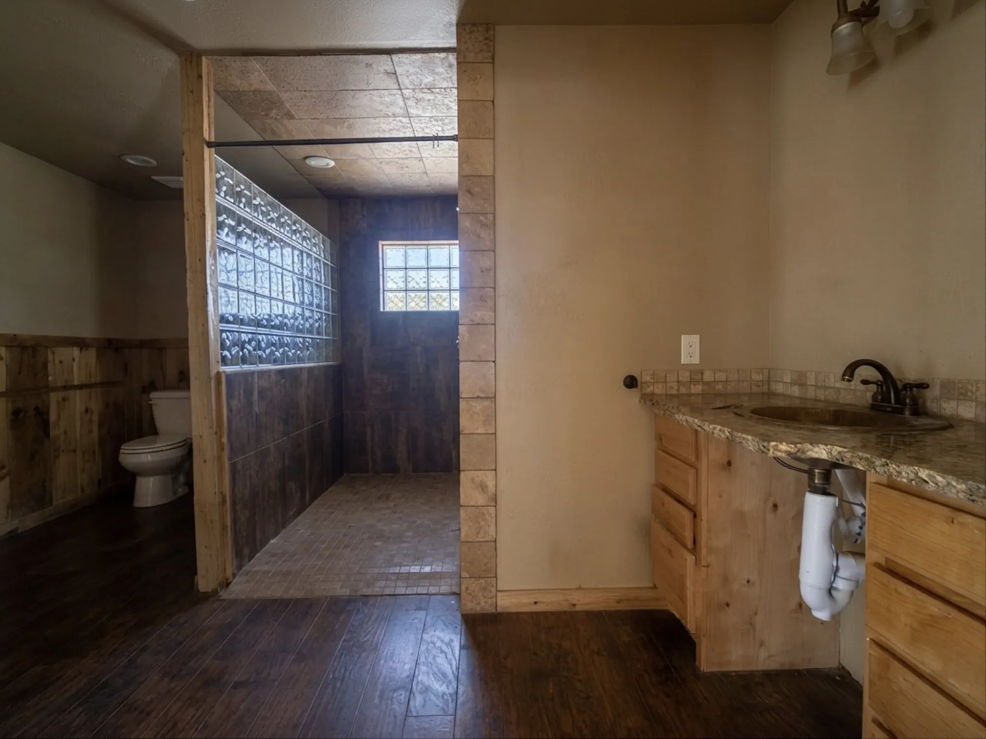 Wood-finish flooring, a vanity with stone countertop, and a walk-in shower with glass block accents