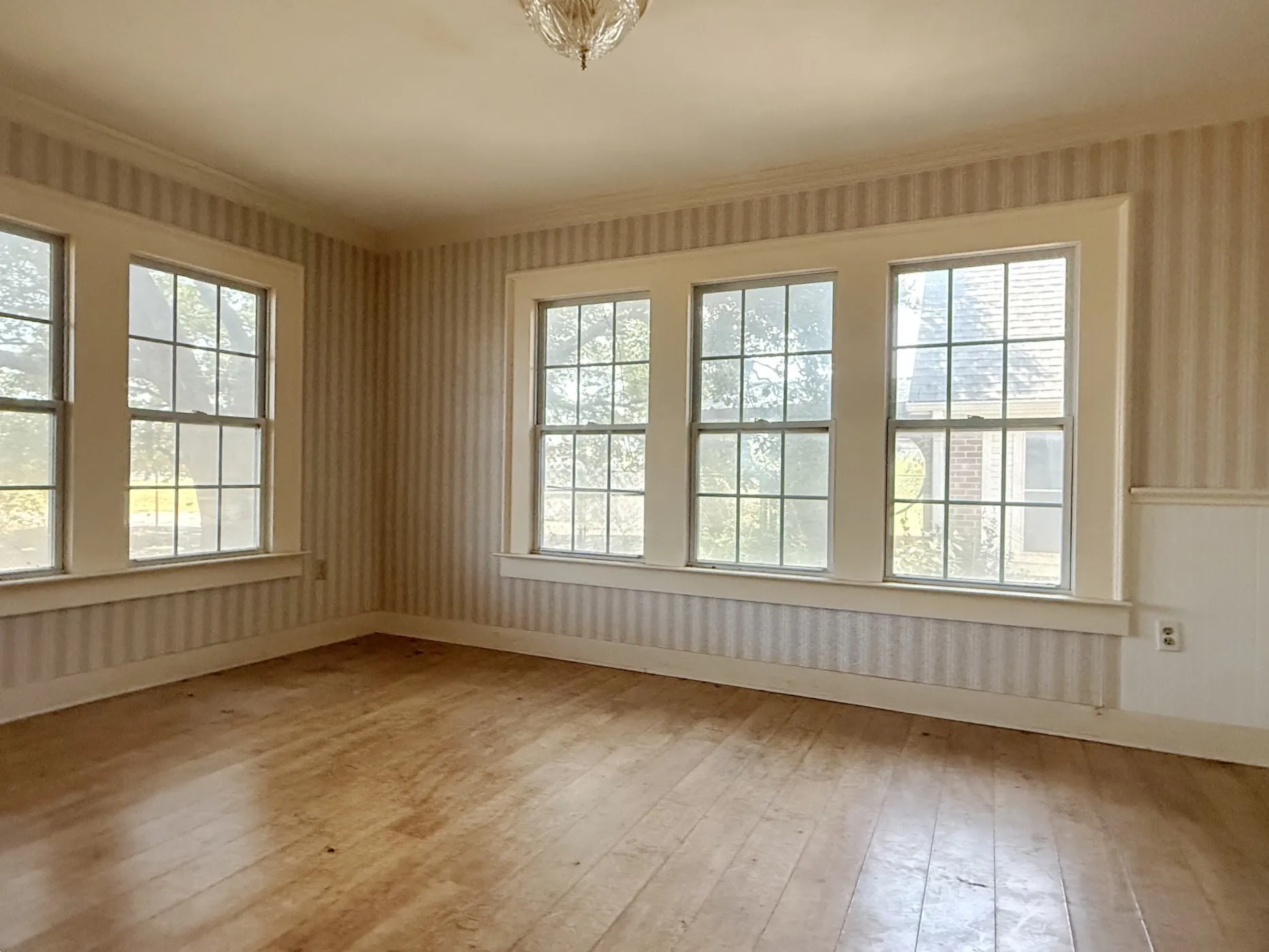 Wood-finish flooring, multiple pane windows, striped wallpaper, wainscoting, and a ceiling-mounted light fixture