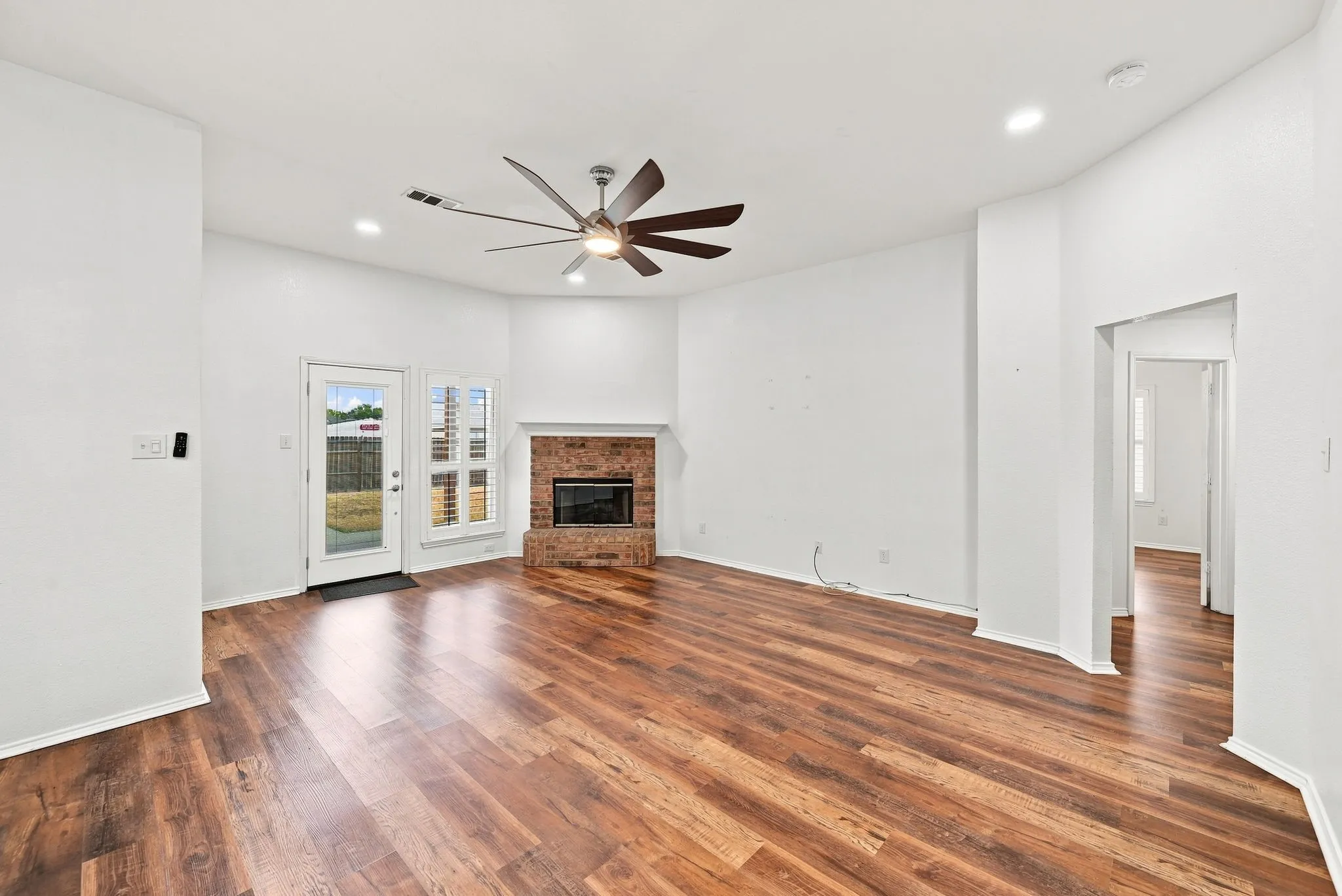Wood-finish flooring, brick fireplace, recessed lighting, ceiling fan, and a glass-paneled door