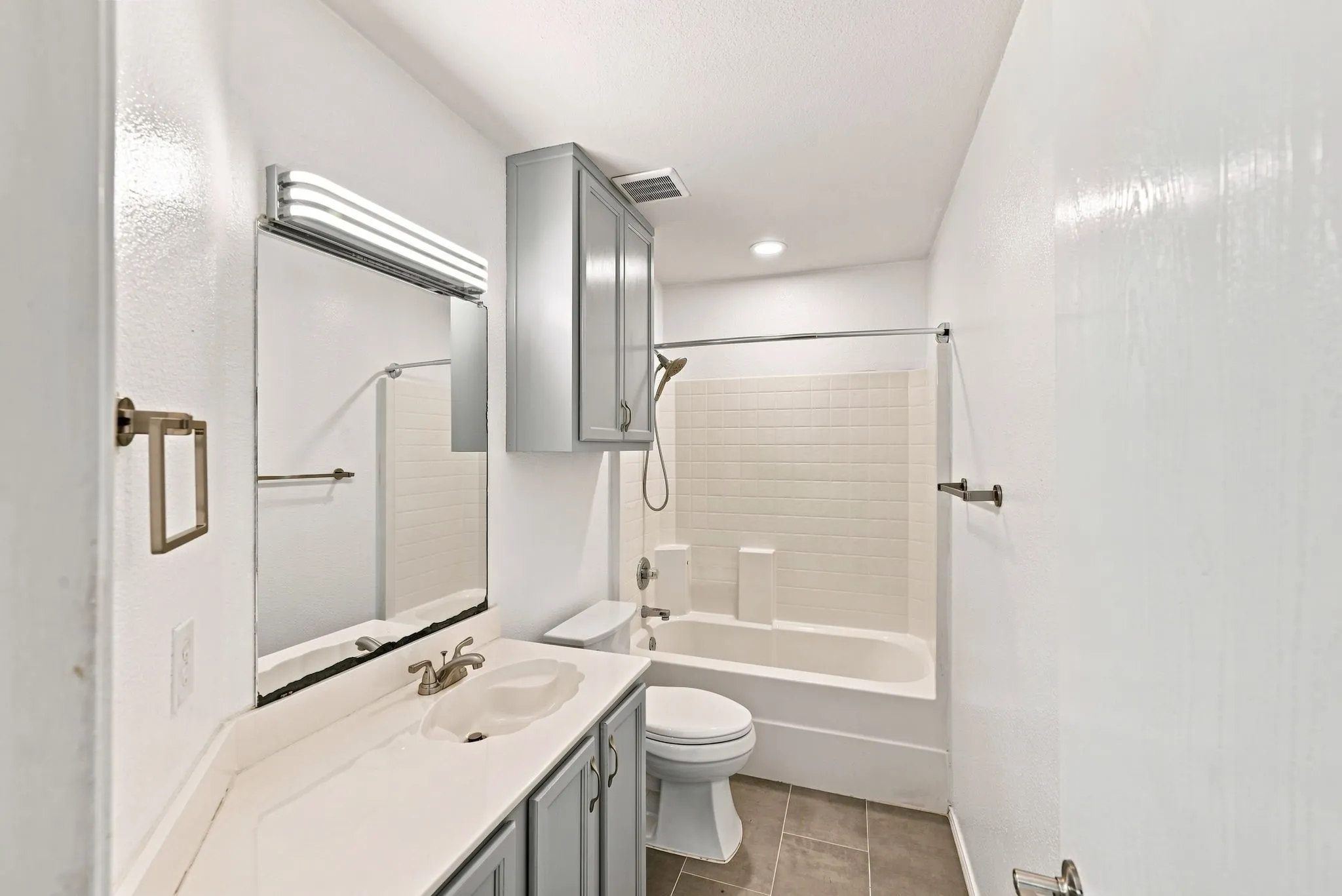 Vanity with integrated sink, rectangular mirror, full bathtub with subway tile surround, and tile flooring