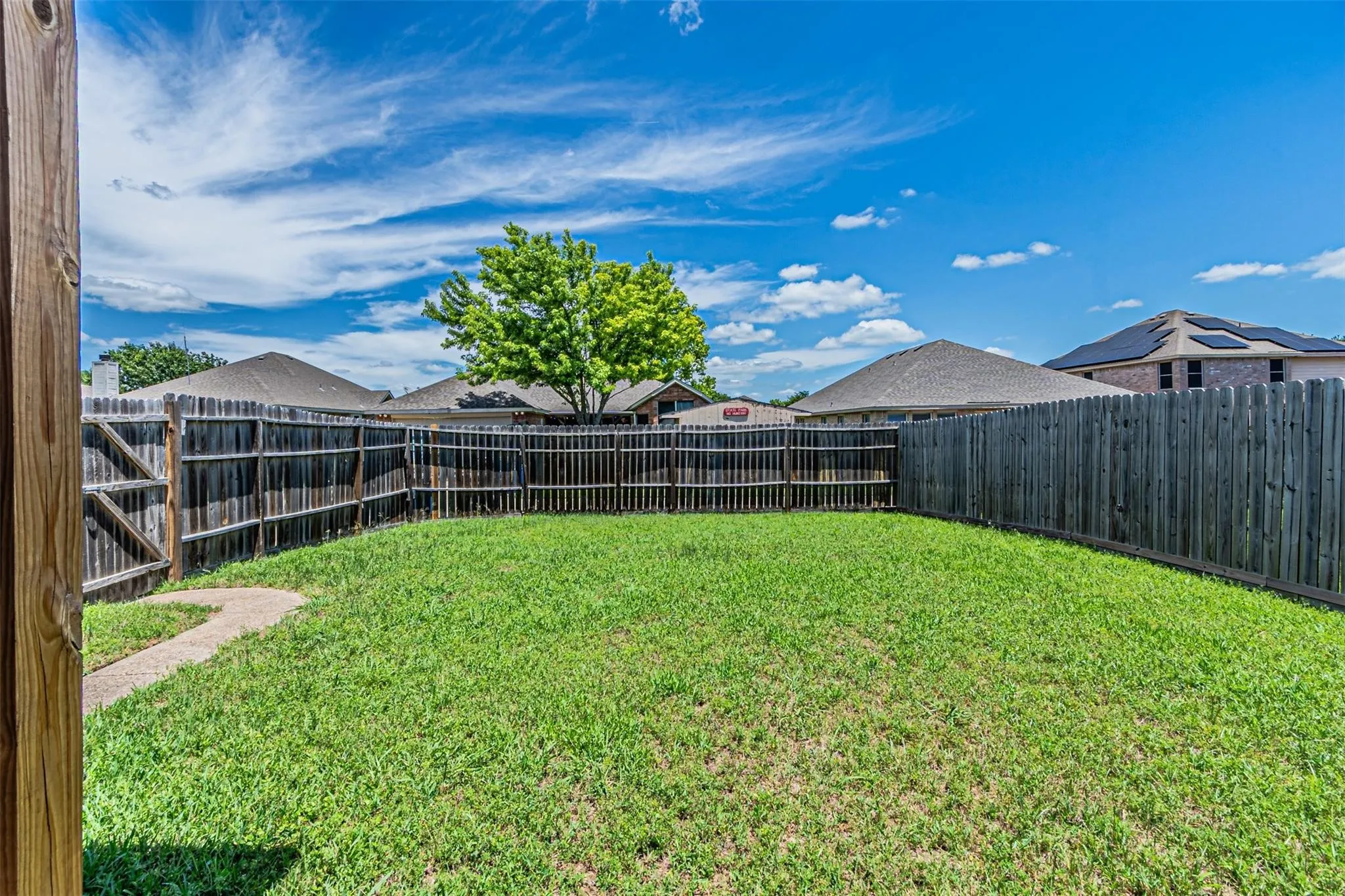 Expansive fenced backyard with a manicured lawn and a curved concrete path