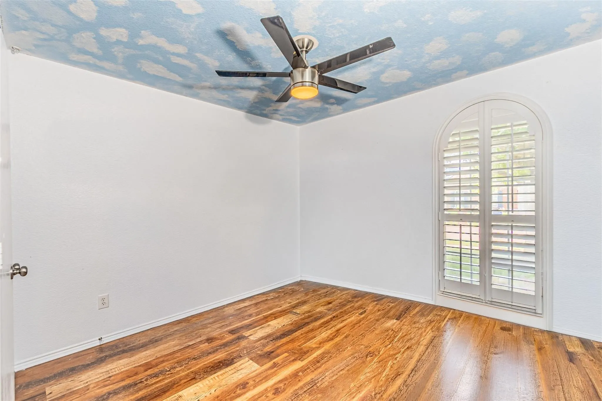 Wood-finish flooring, white walls, and an arched window with plantation shutters