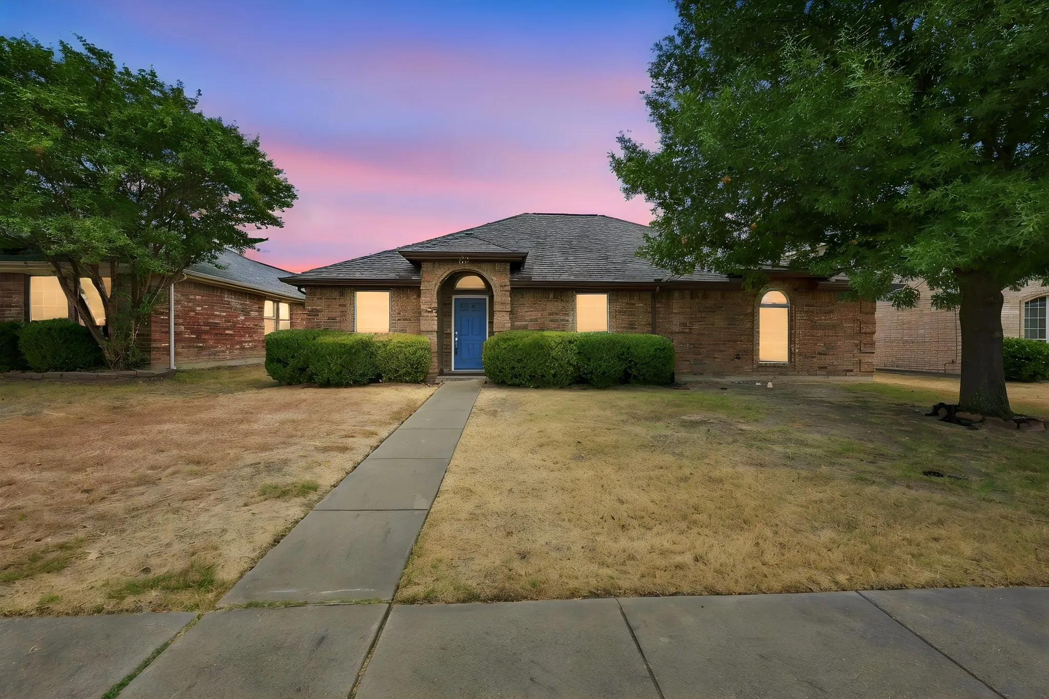 Brick exterior with a prominent arched entry, a blue front door, mature trees, and established shrubs