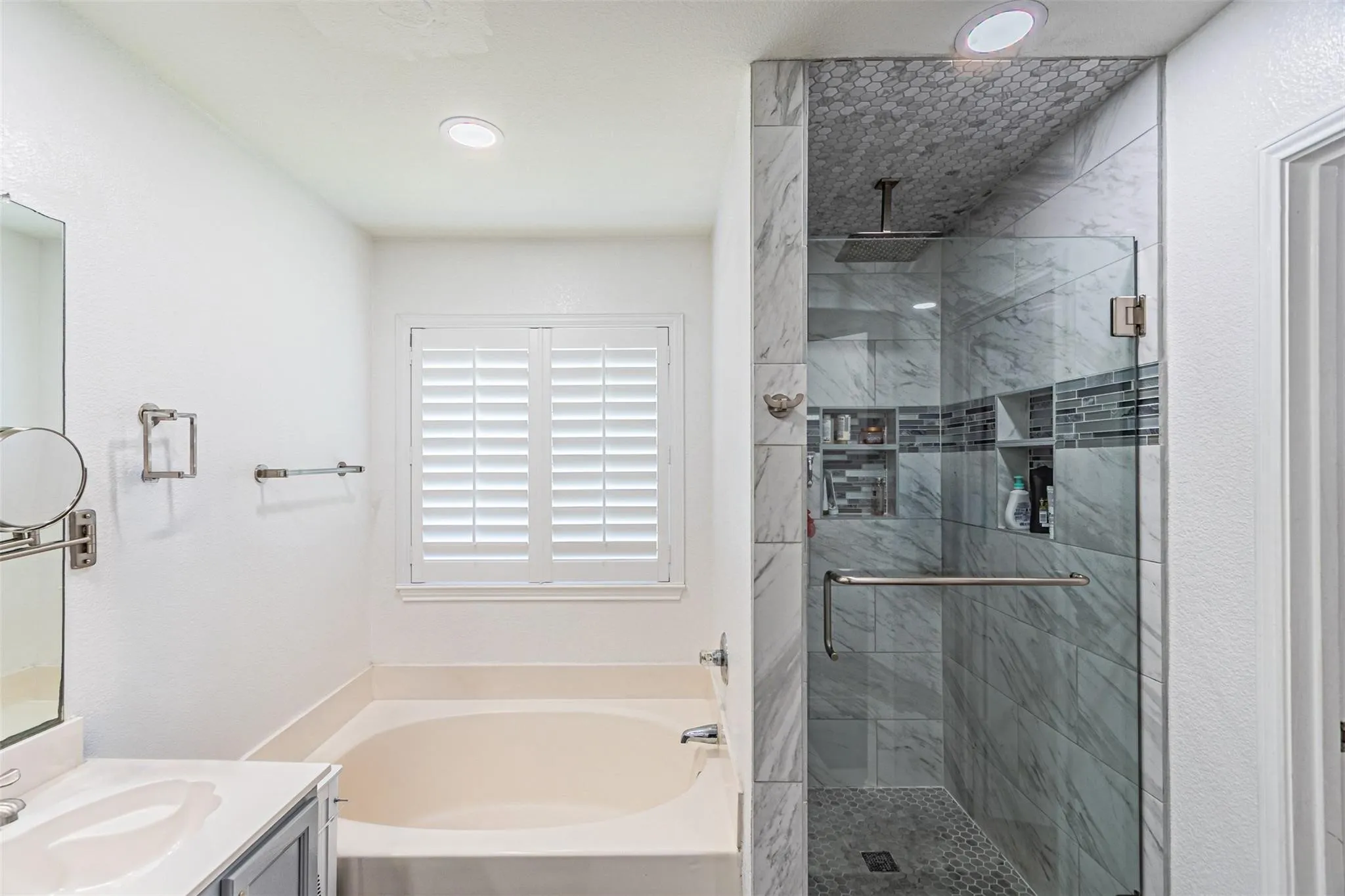 Walk-in shower with glass enclosure, marble-patterned tile, and recessed shelving