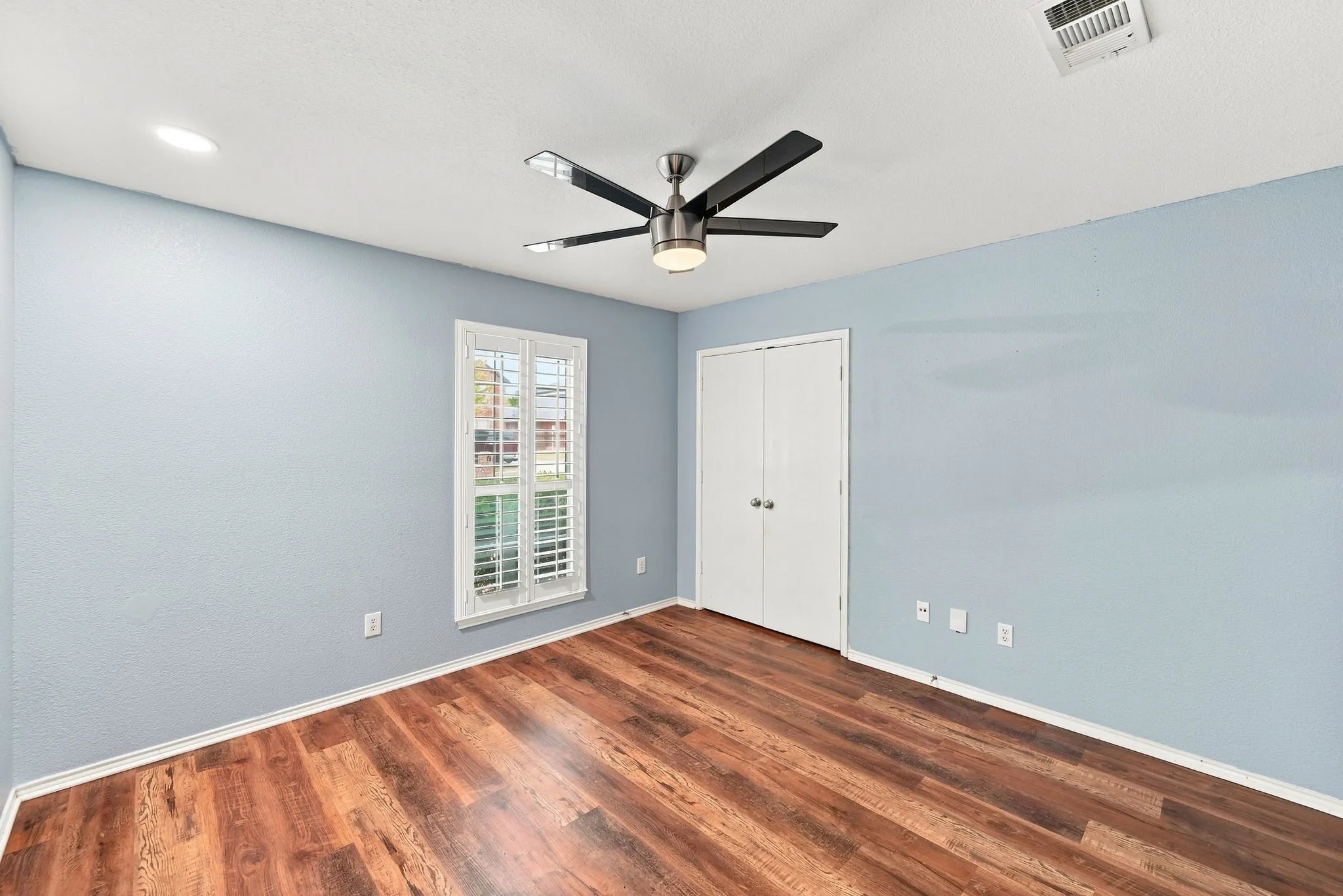 Wood-finish flooring, ceiling fan with integrated lighting, recessed lighting, double-door closet, and window with plantation shutters