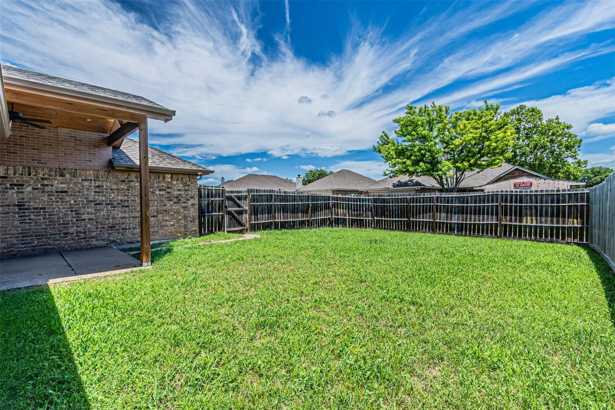 Expansive backyard featuring a covered patio with wood beam accents, brick exterior, and a privacy fence