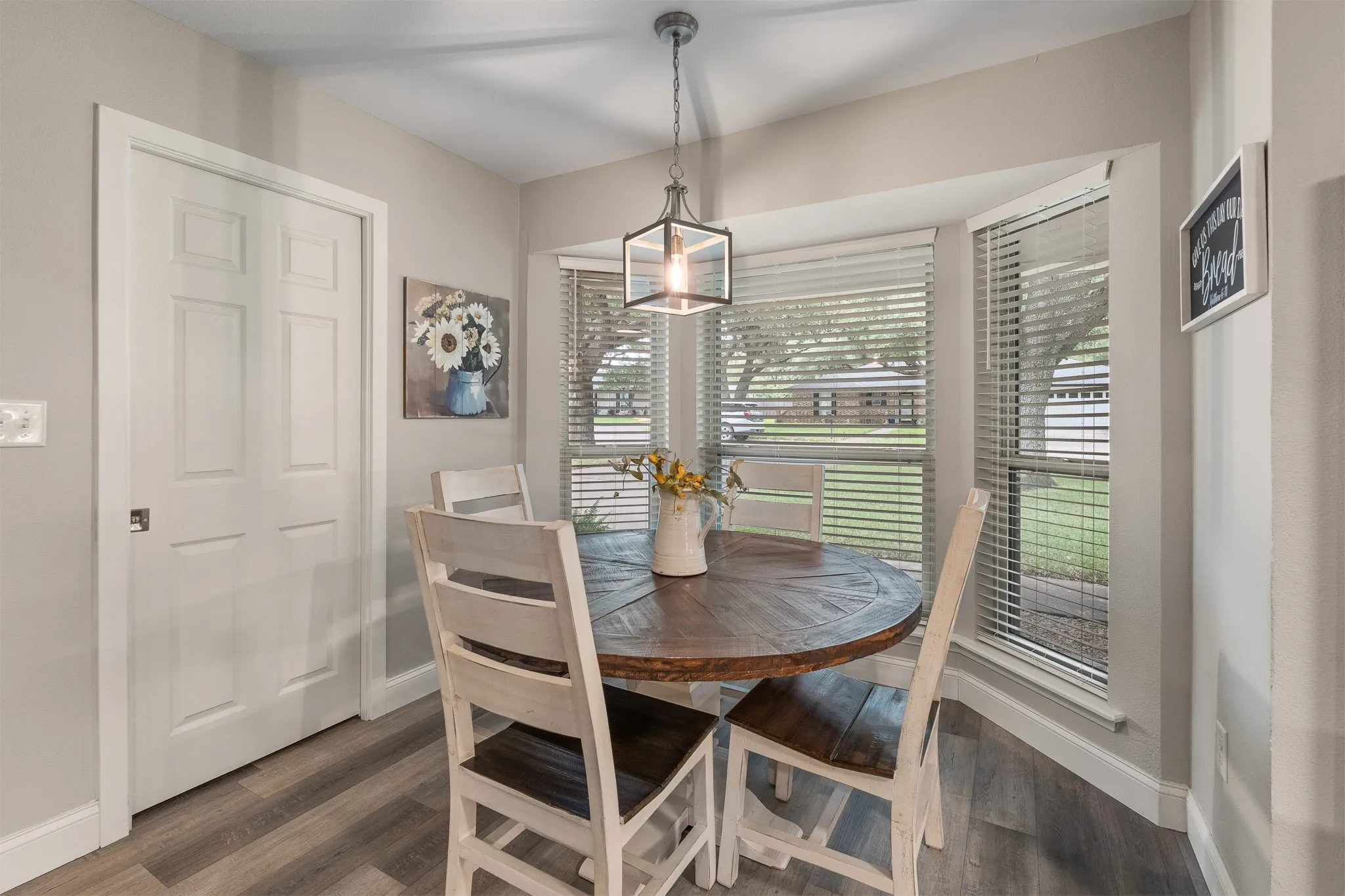 Bay window with blinds, wood-finish flooring, and a modern pendant light fixture