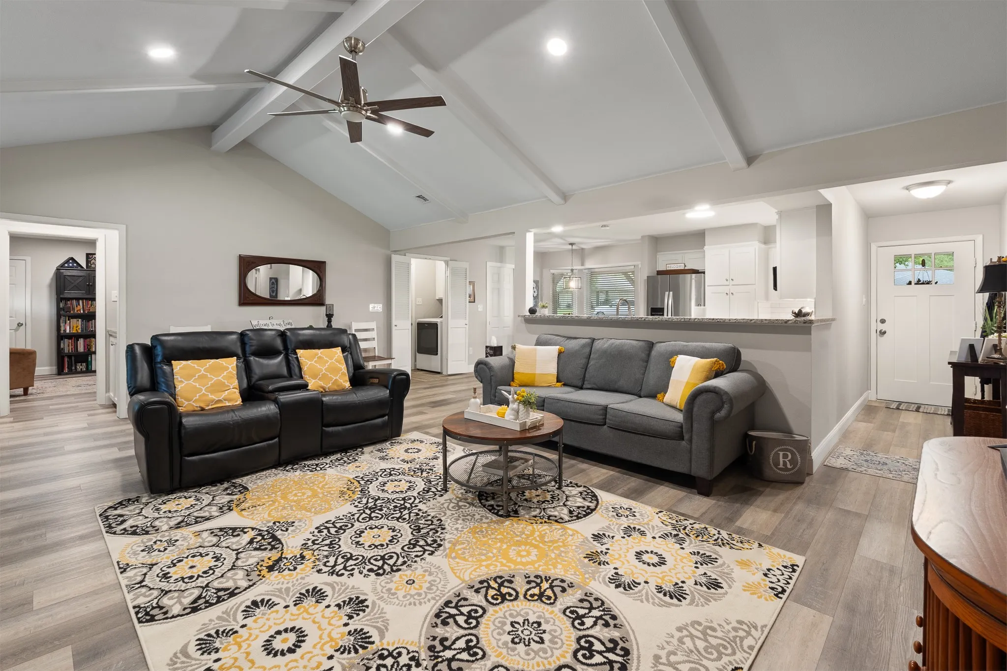 Vaulted ceiling with exposed beams, recessed lighting, wood-finish flooring, and a kitchen pass-through with a stone-finish countertop