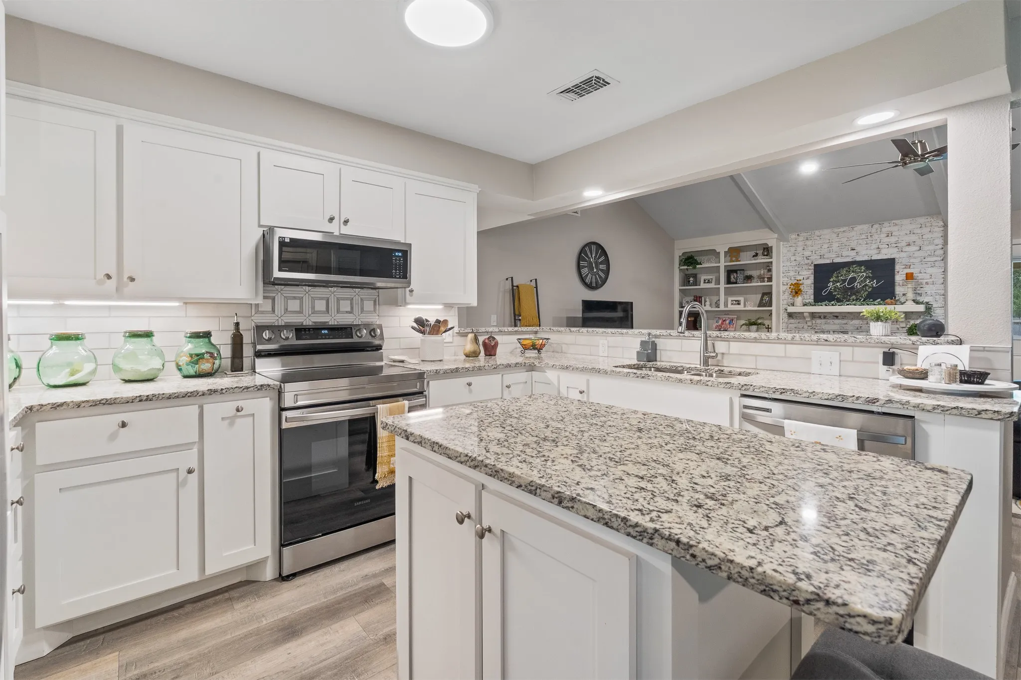 White cabinetry, an island with stone countertops, a stainless steel appliance suite, wood-finish flooring, and recessed lighting