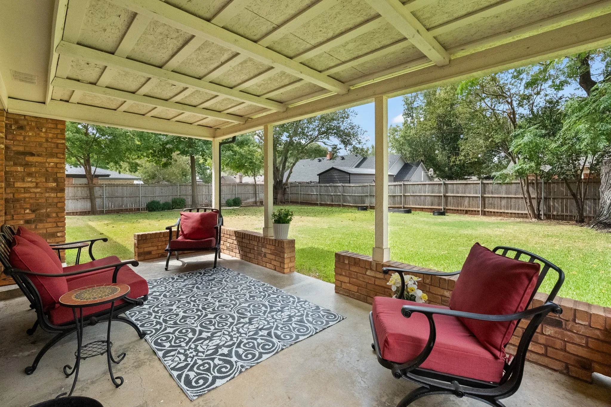 Covered patio with a concrete surface, brick half-walls, and a wood-paneled ceiling