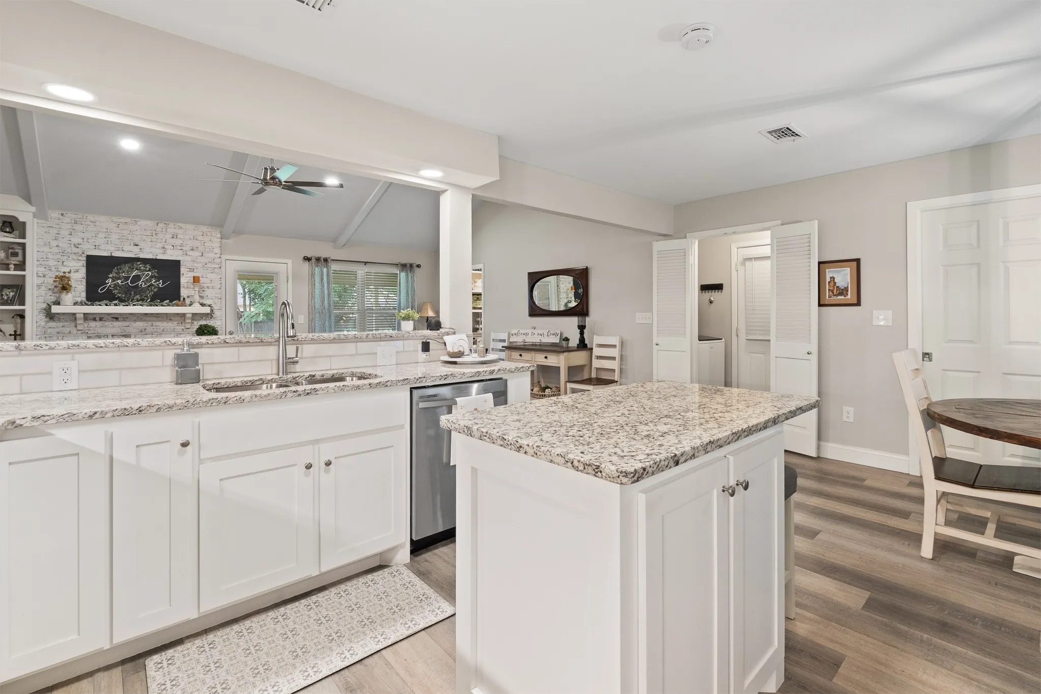 White cabinetry, granite countertops, white subway tile backsplash, stainless steel dishwasher, and wood-finish flooring