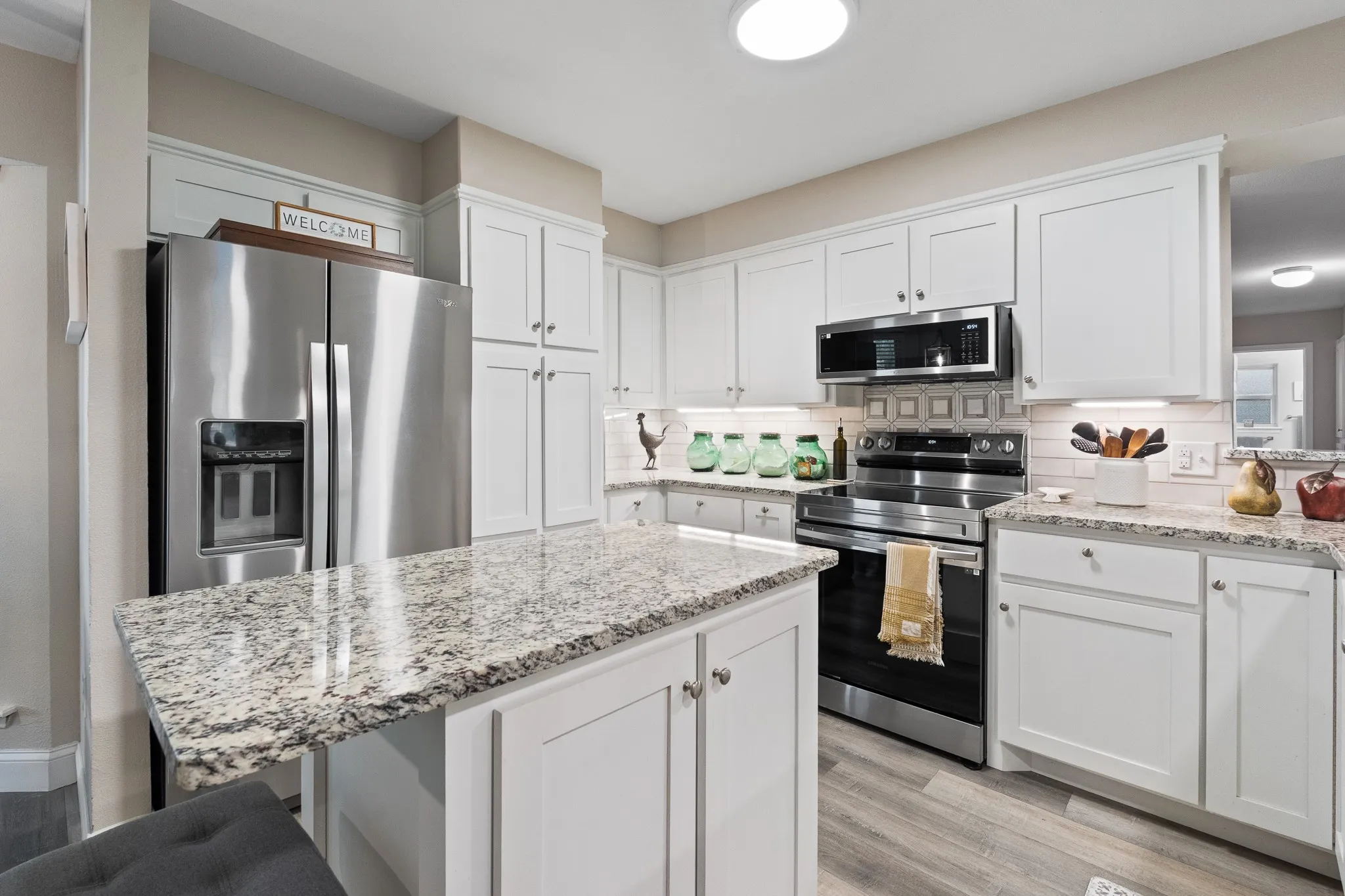 Kitchen featuring white cabinetry, light-toned countertops, stainless steel appliances, and wood-finish flooring