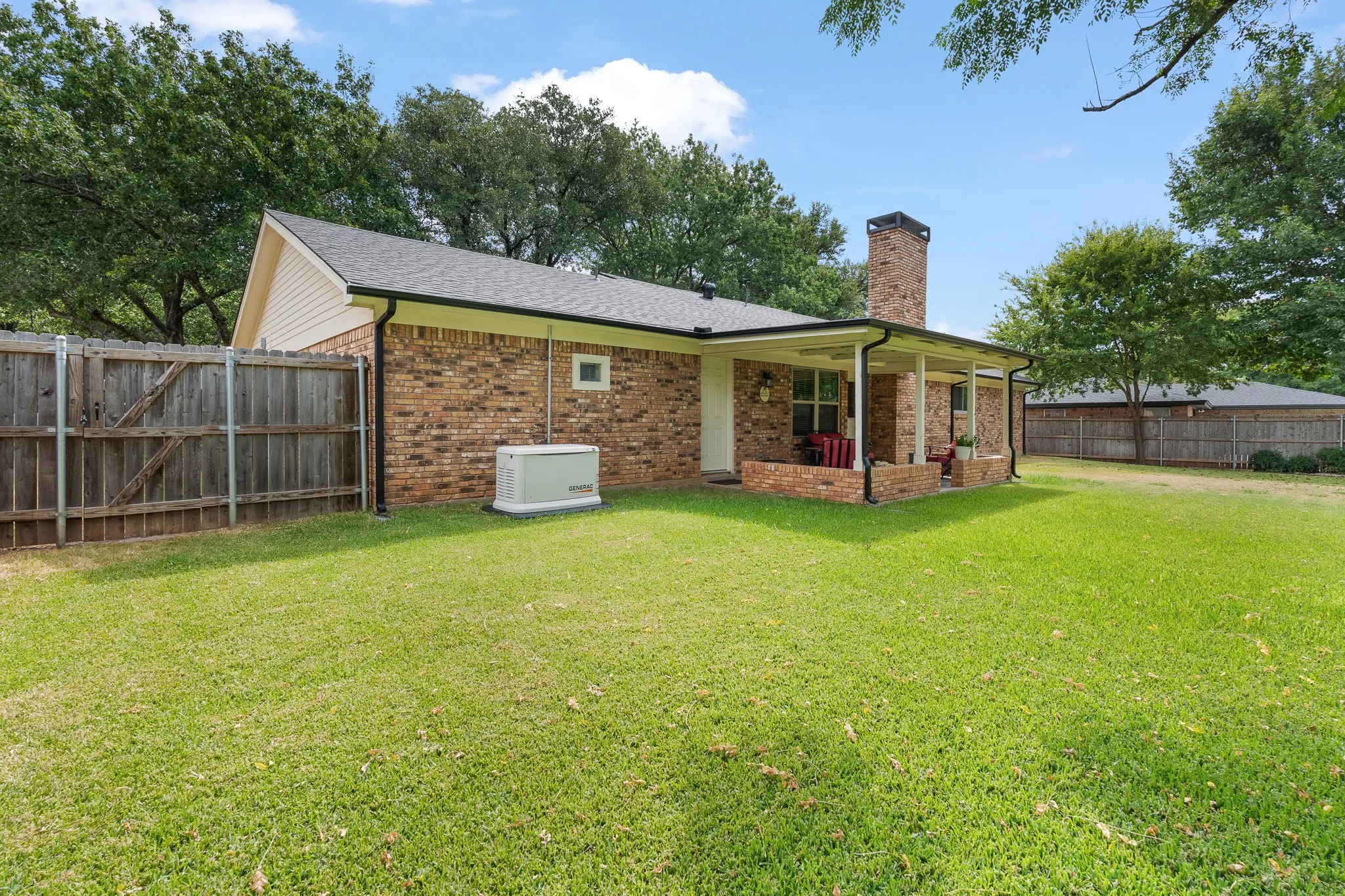 Brick exterior with a covered patio, a brick chimney, and a black shingle roof
