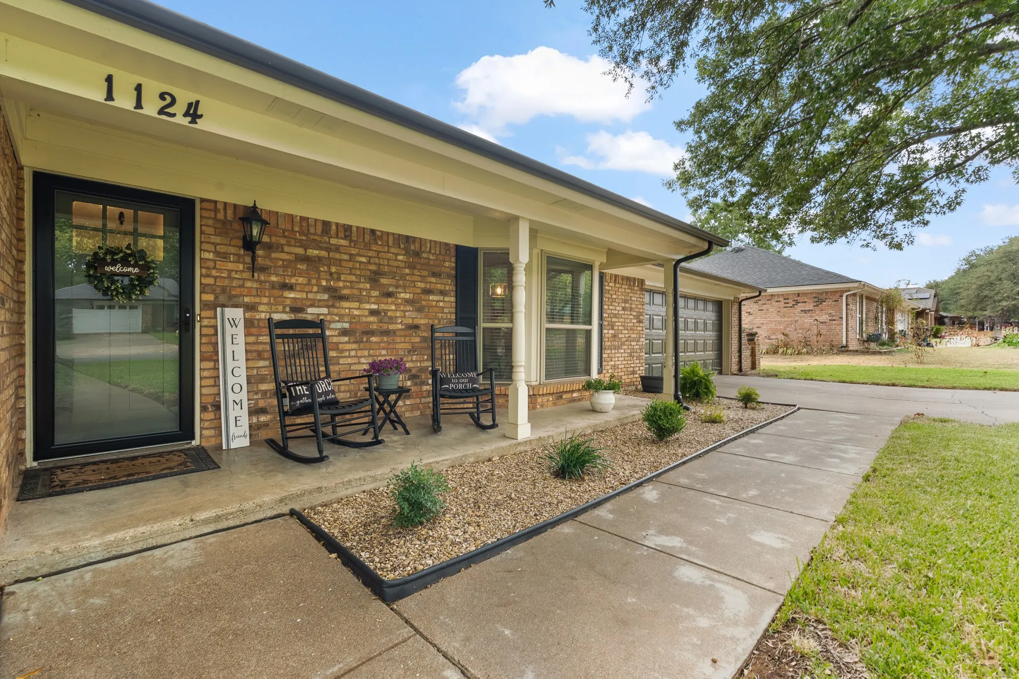 Brick exterior featuring a covered porch, detached garage with glass-paneled doors, and a concrete pathway